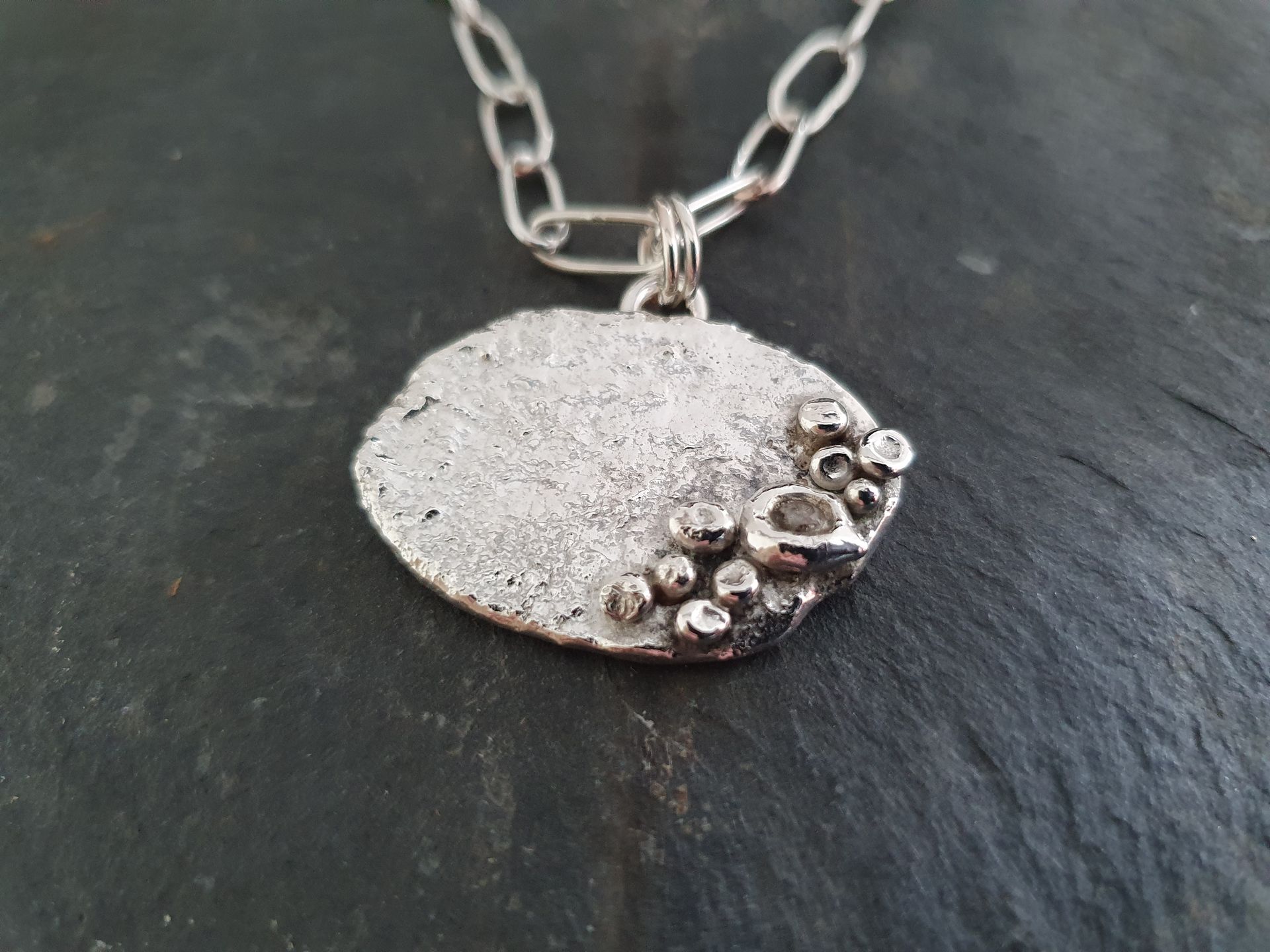 Zilveren hanger met ovale hanger en ketting met textuur.