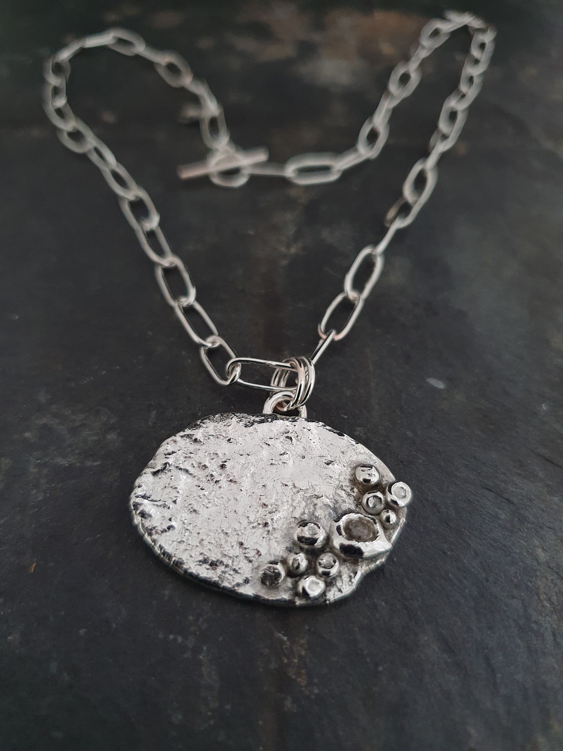 Zilveren hanger met ovale hanger en ketting met textuur.