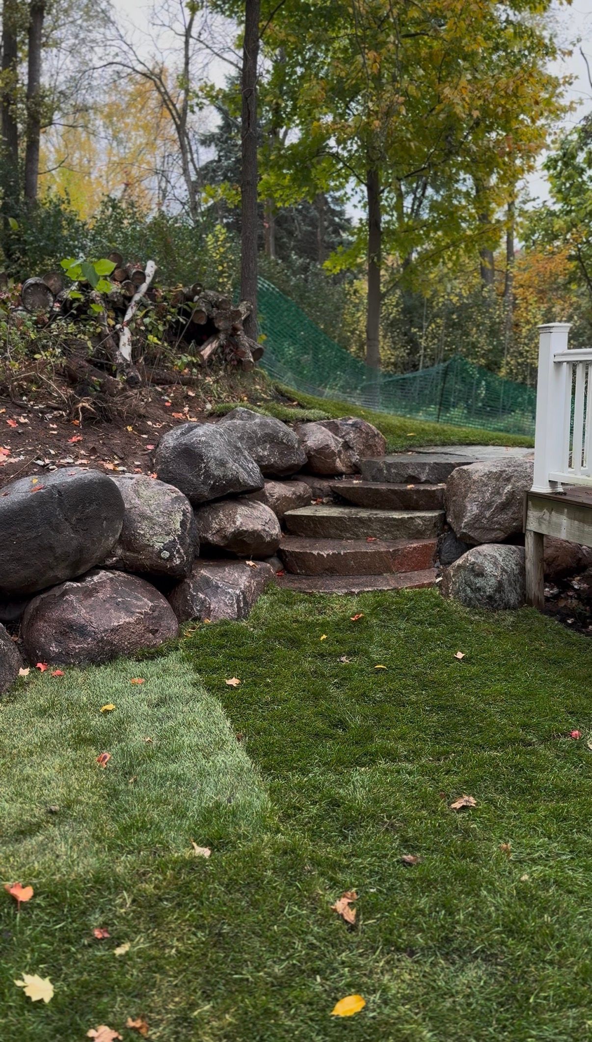 Stone steps set into a garden hill beside a white railing, surrounded by trees and a green lawn.