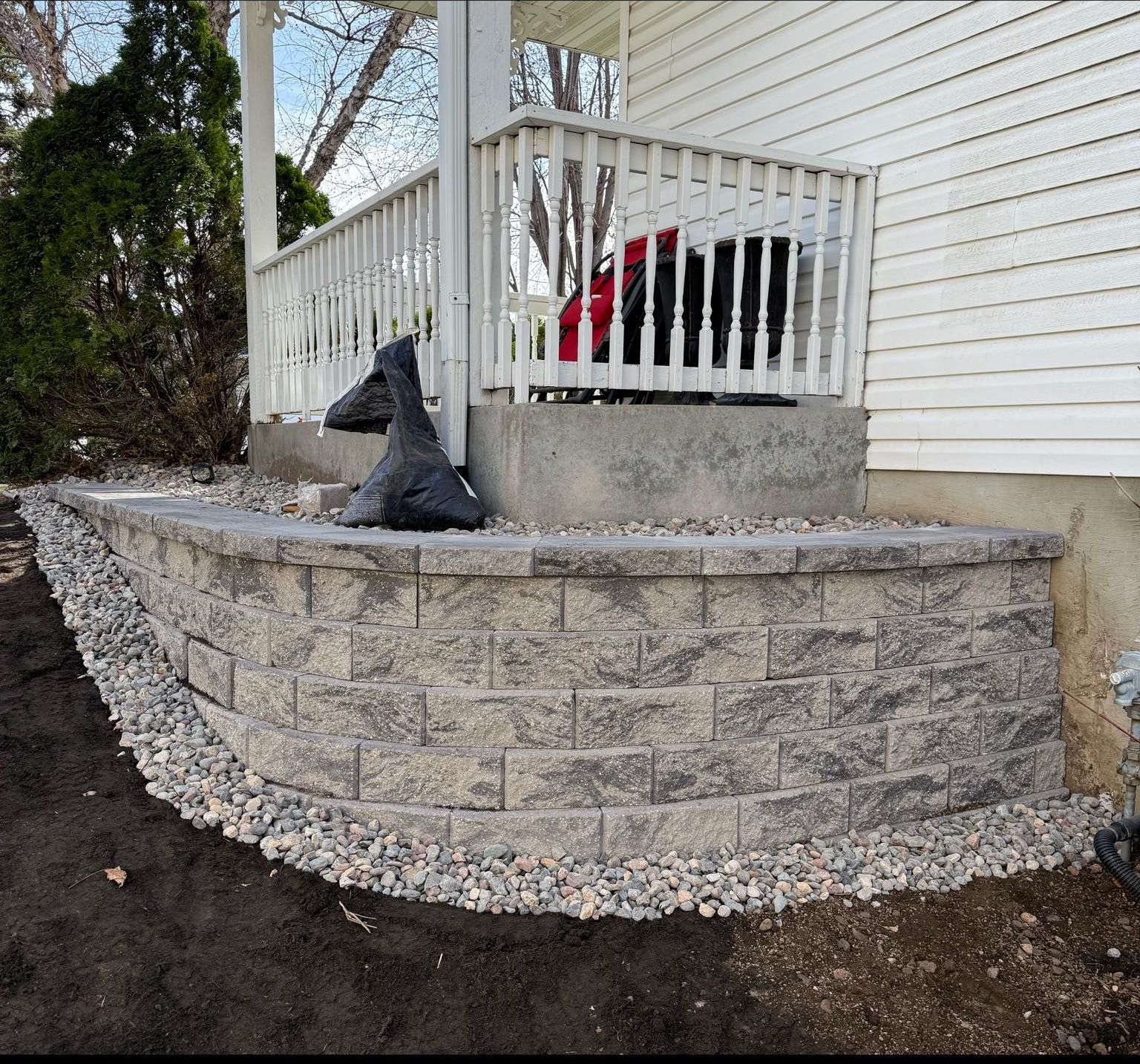 A curved concrete retaining wall with a gravel border in front of a white porch and house.