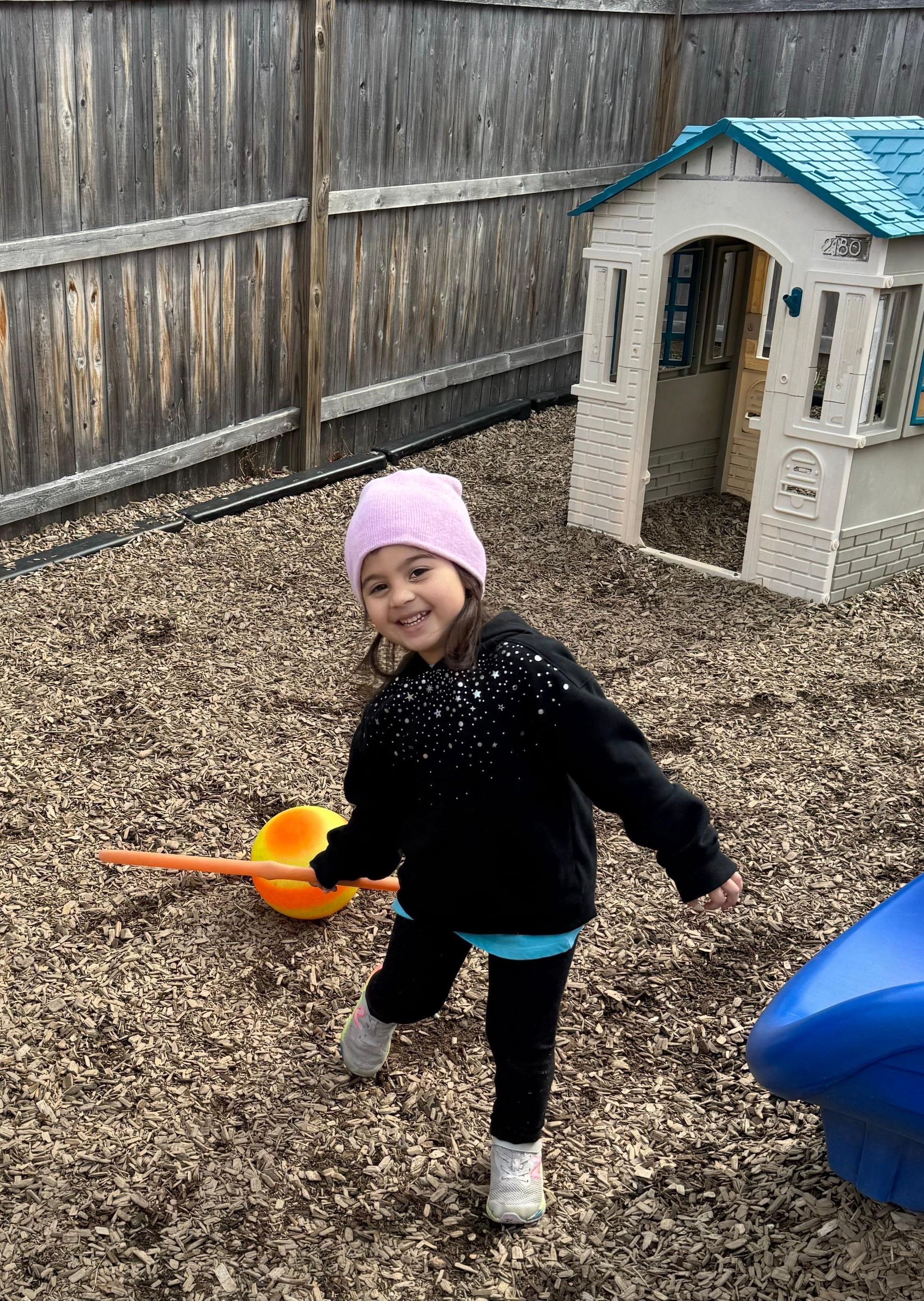 A little girl is standing in front of a playhouse in a playground.