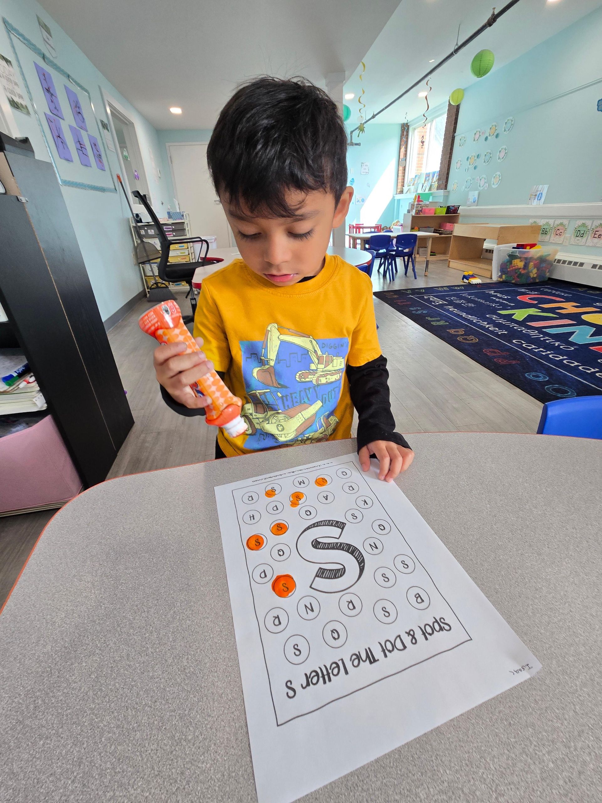 A young boy is sitting at a table holding an orange marker.