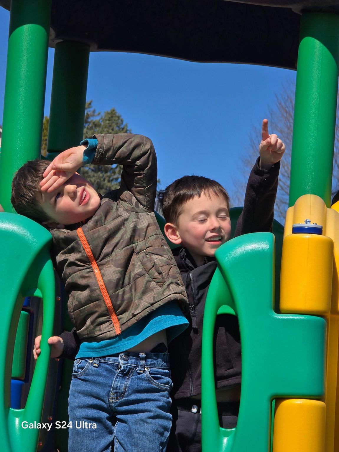 Two young boys are playing on a playground with a galaxy s24 ultra in the background
