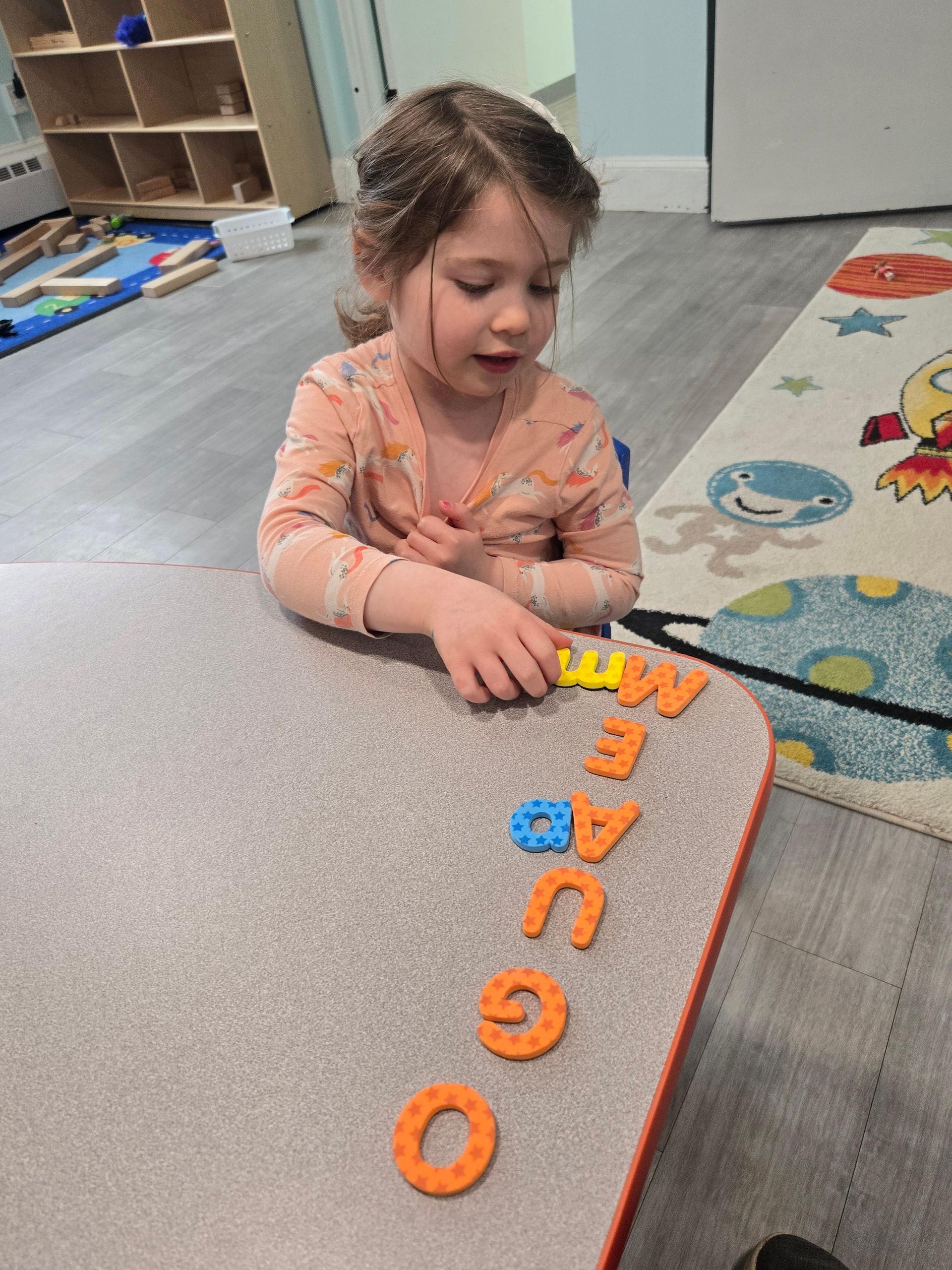 A little girl is sitting at a table playing with letters.
