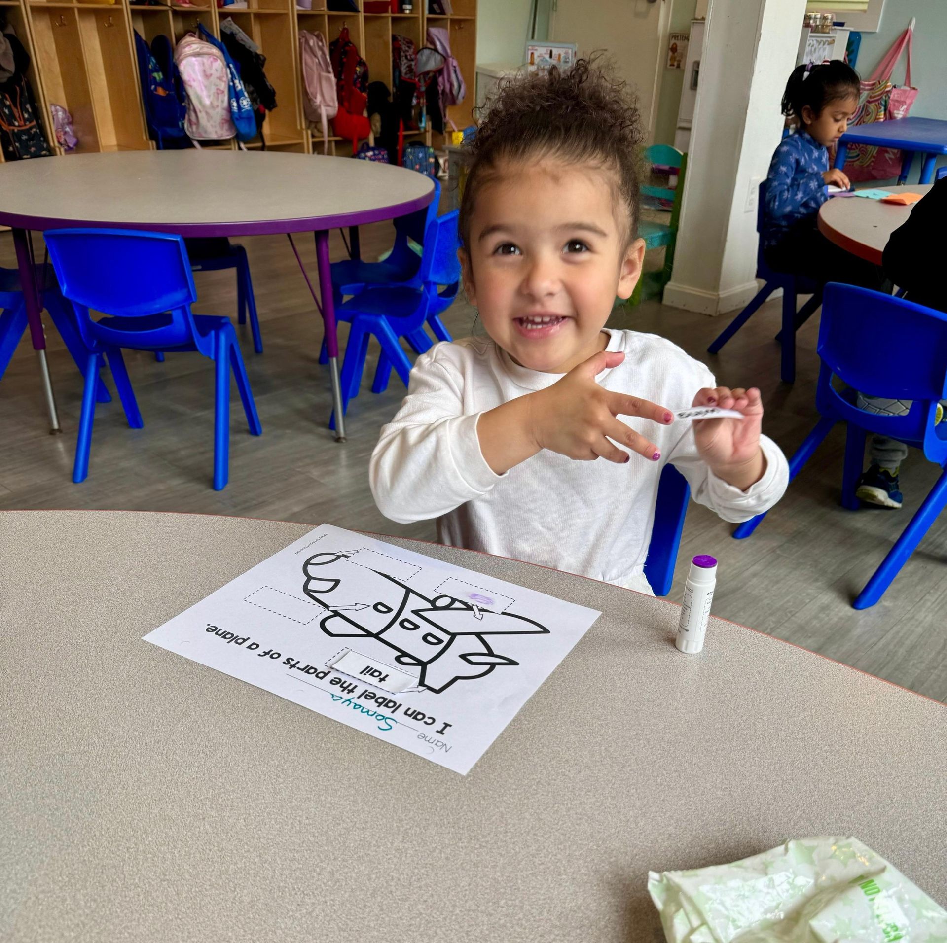 A little girl is sitting at a table with a marker in her hand.