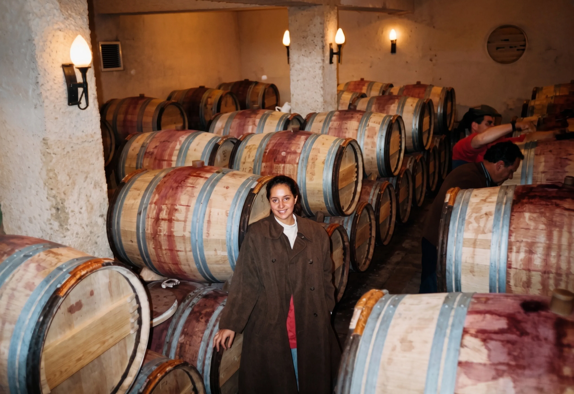 Una persona de pie entre hileras de coloridos barriles de madera en una bodega.