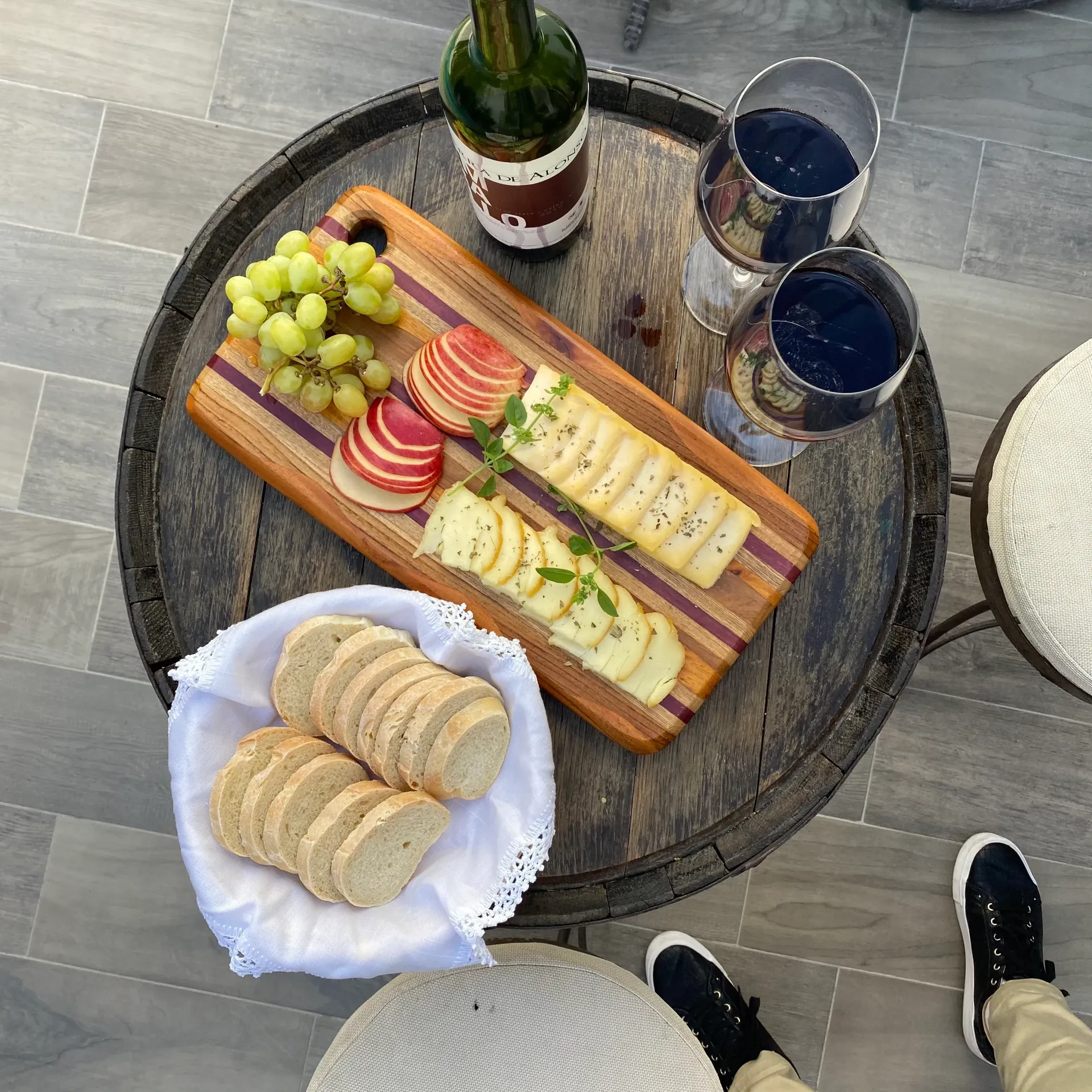 Tabla de embutidos con uvas, queso, galletas saladas y vino en una mesa redonda de patio.