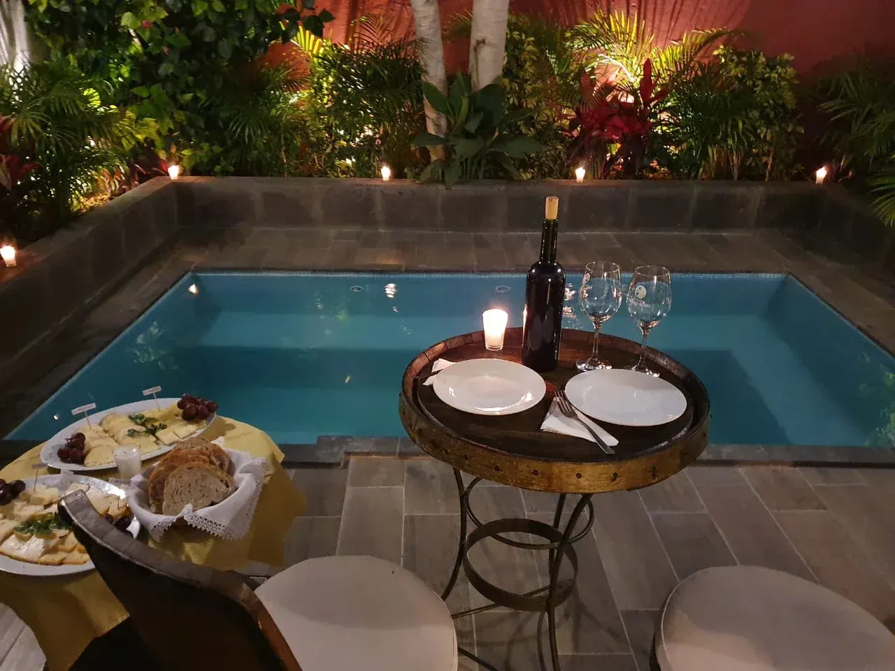 Cenar junto a la piscina con vino y platos al lado de una piscina iluminada por la noche.