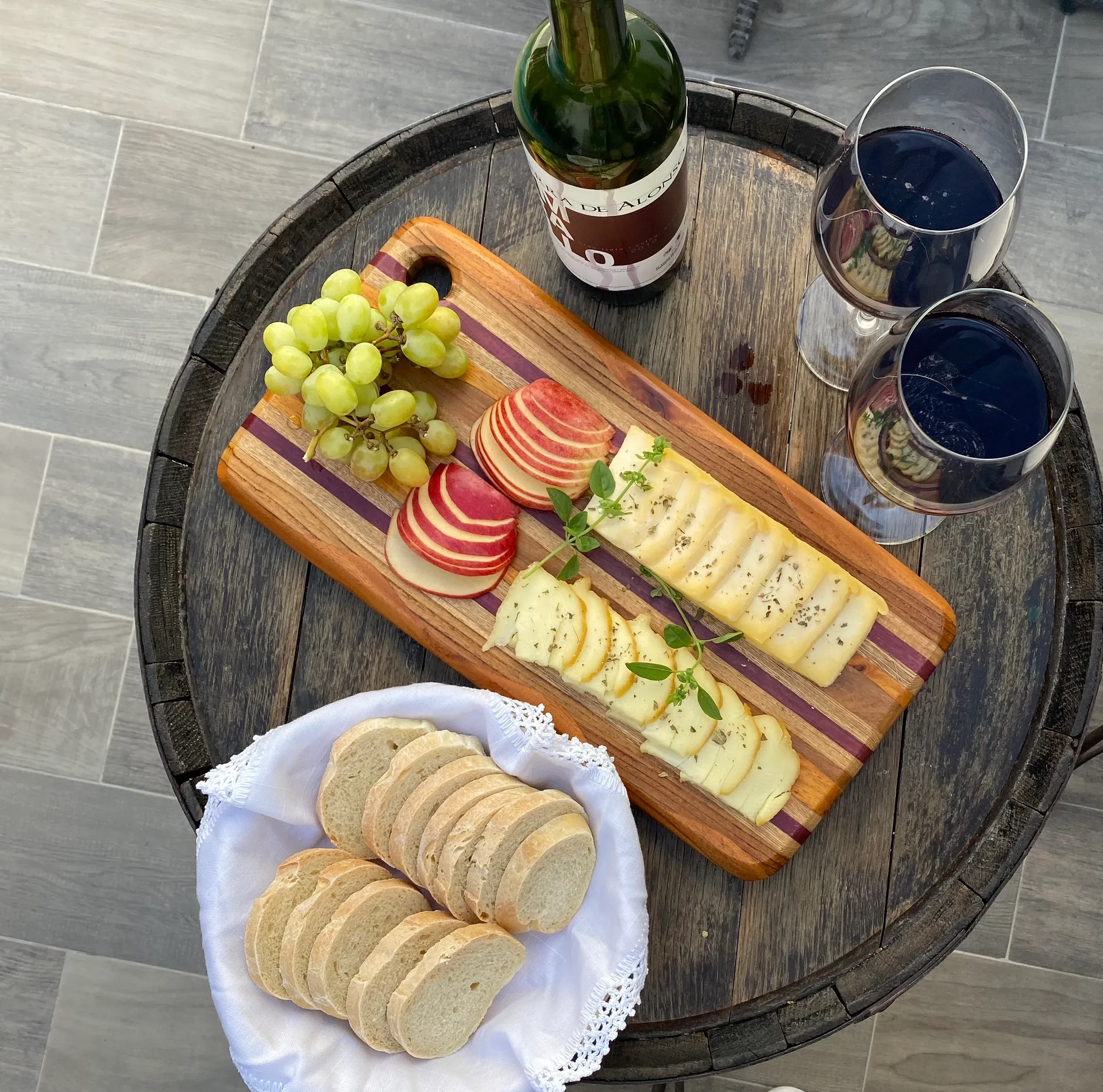 Tabla de vinos y quesos con uvas, galletas saladas, fruta en rodajas y dos copas sobre una mesa redonda.