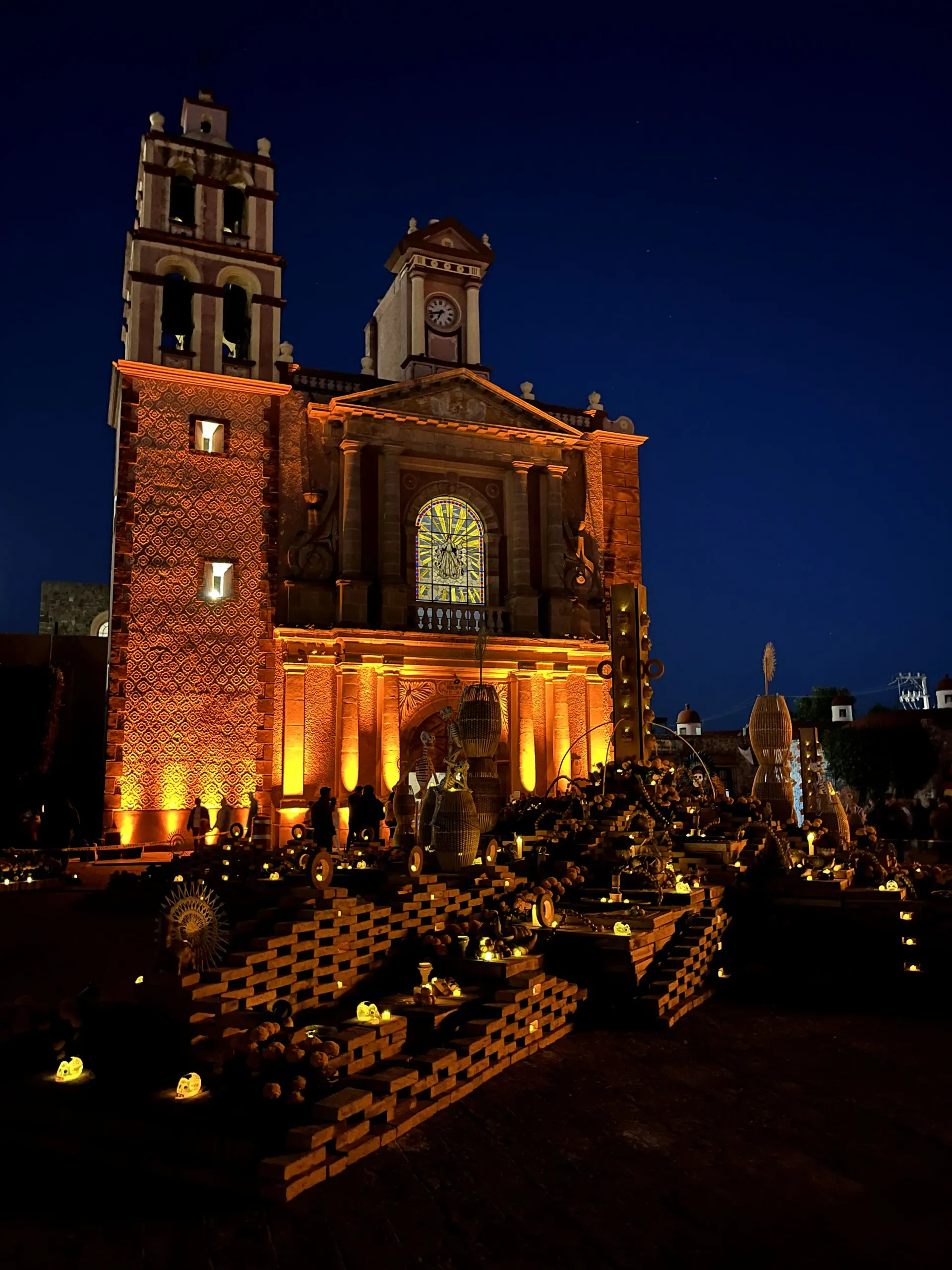 Illuminated stone church at night with warm lights and a blue sky, surrounded by flowers and steps