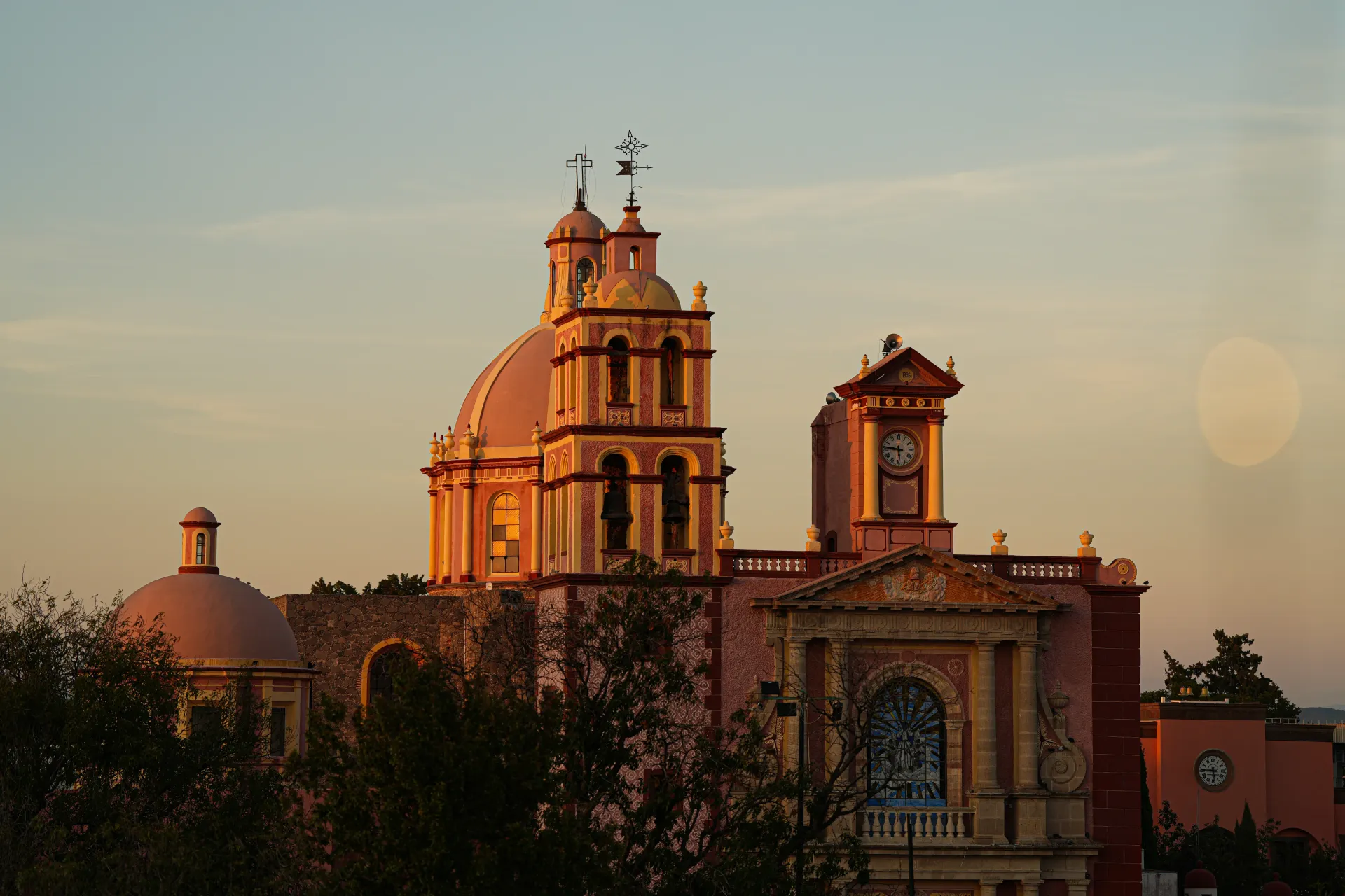 Sunlit historic church with twin towers at sunset, framed by trees and a clear sky