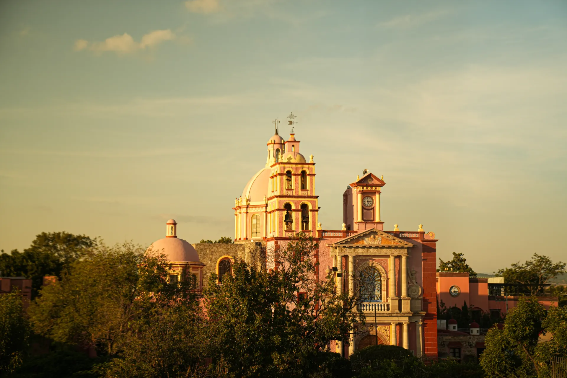 Sunlit historic cathedral and bell tower above trees under a clear sky