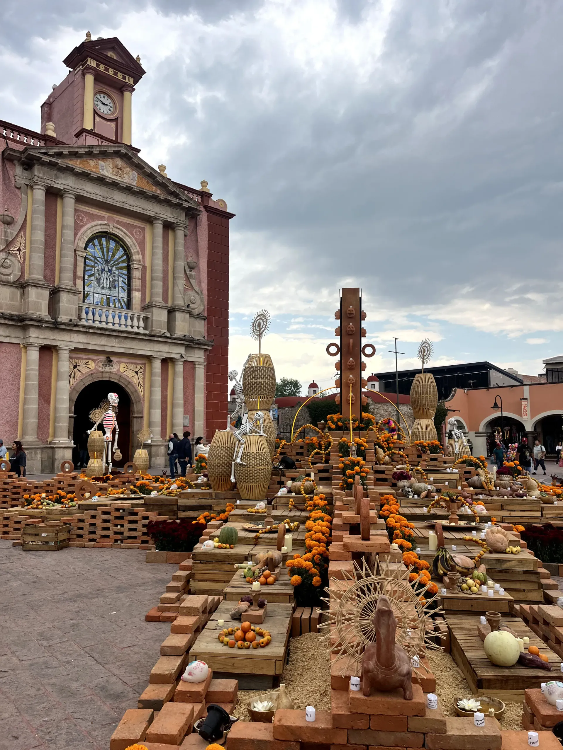 Altar al aire libre del Día de Muertos con caléndulas, velas, pan y una fachada de iglesia ornamentada al fondo.