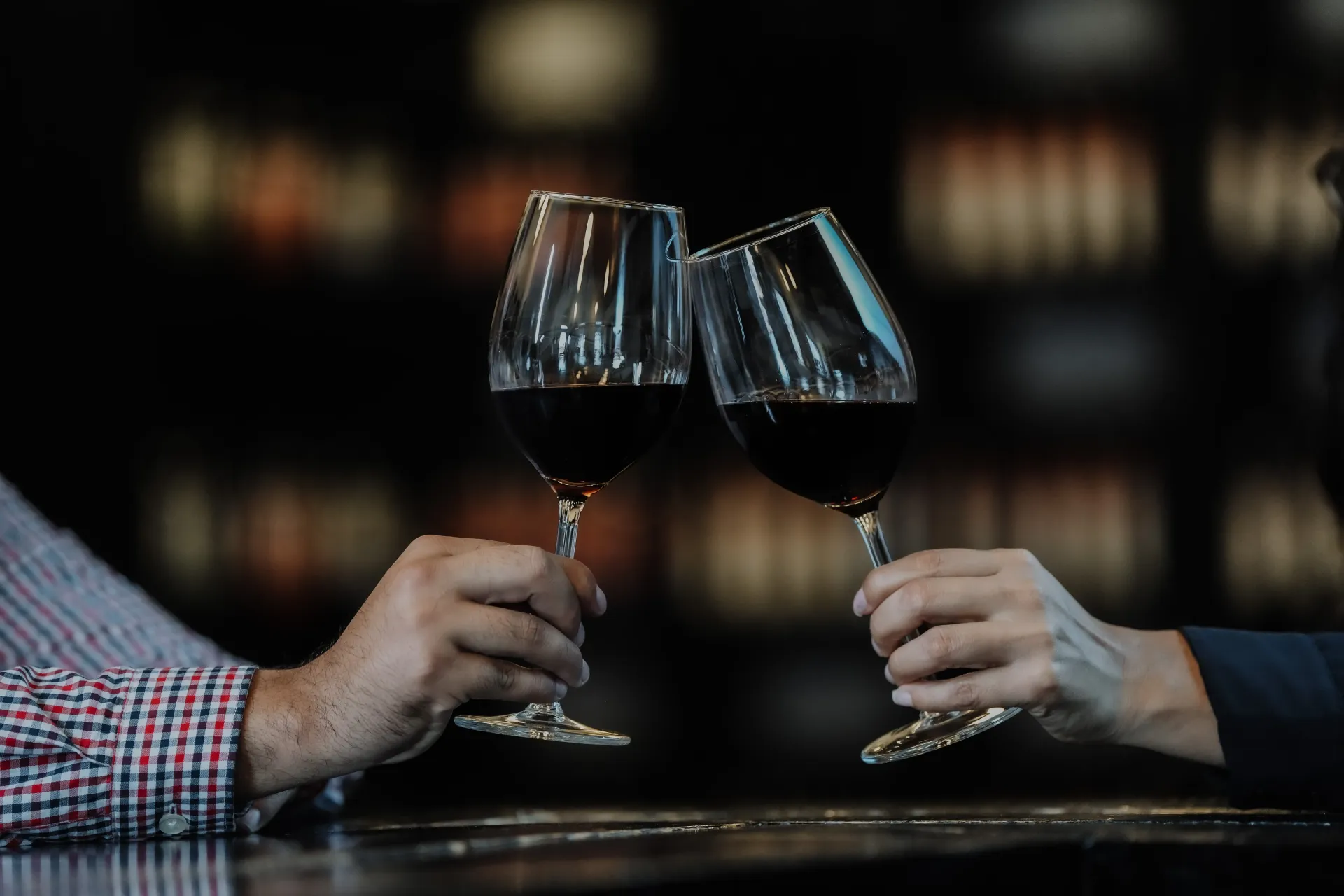 Dos personas chocan sus copas de vino tinto en un bar con poca luz.