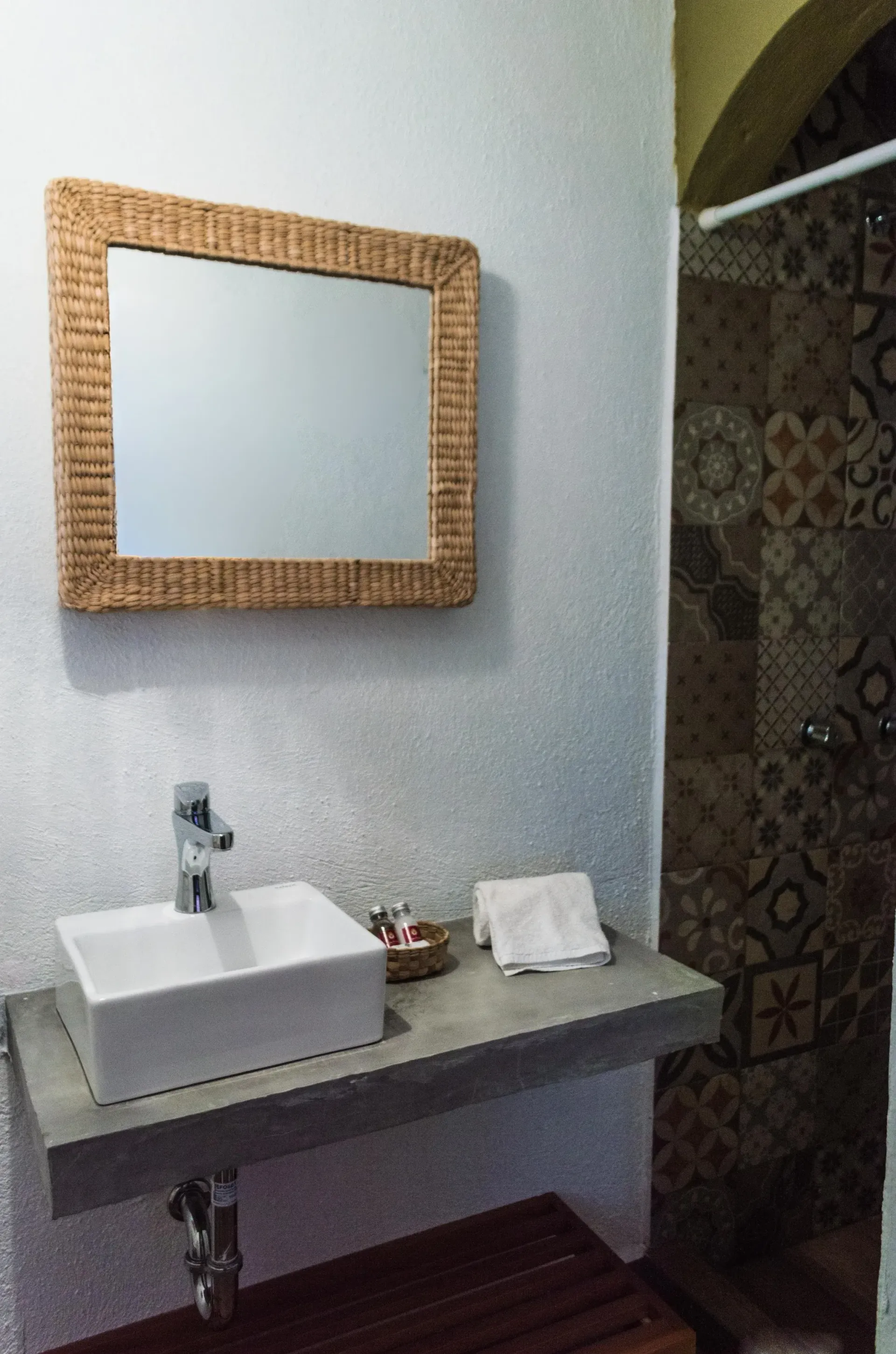 Modern bathroom vanity with rectangular sink, mirror, gray counter, and patterned shower curtain.