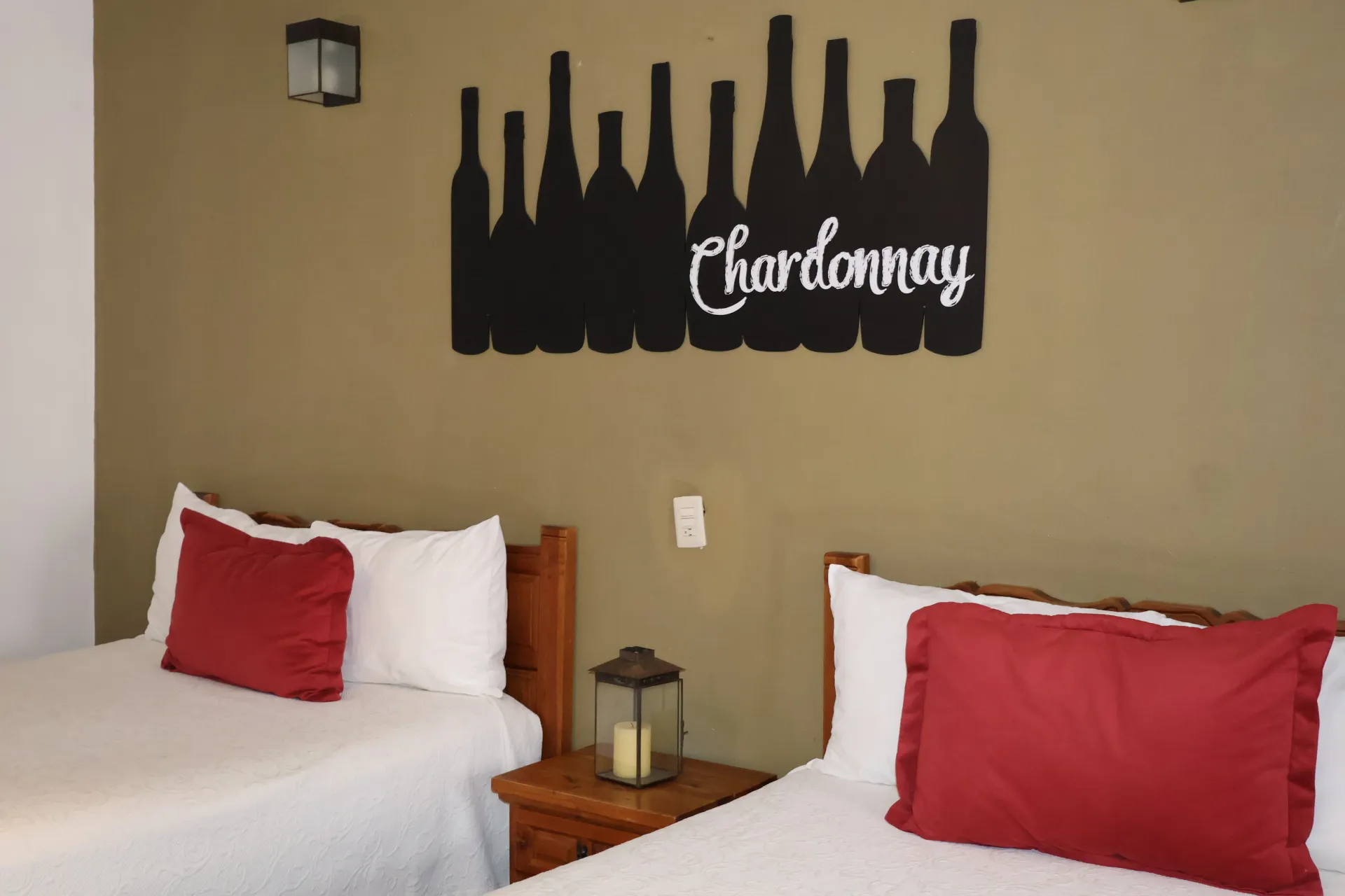 Bedroom with two twin beds, red pillows, and a black Chardonnay wine bottle wall decor above the headboard
