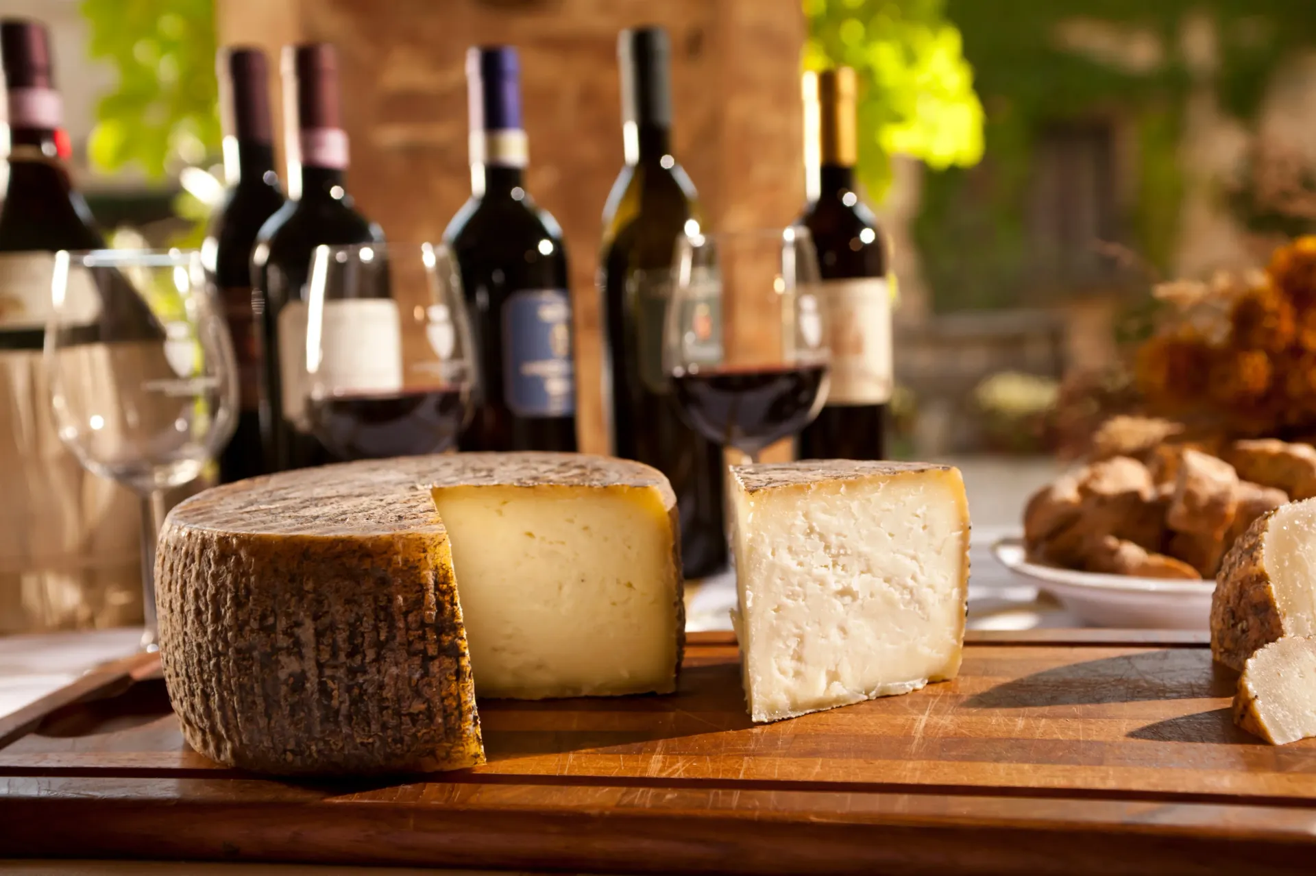 Queso sobre una tabla de madera con botellas de vino y una copa en un ambiente rústico.