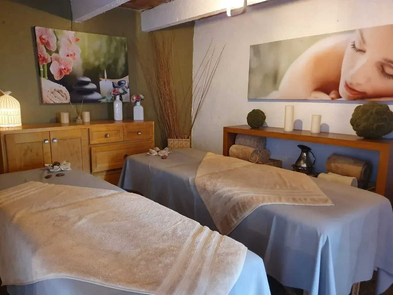 Massage room with two treatment tables, wood cabinets, and serene wall art in soft neutral tones