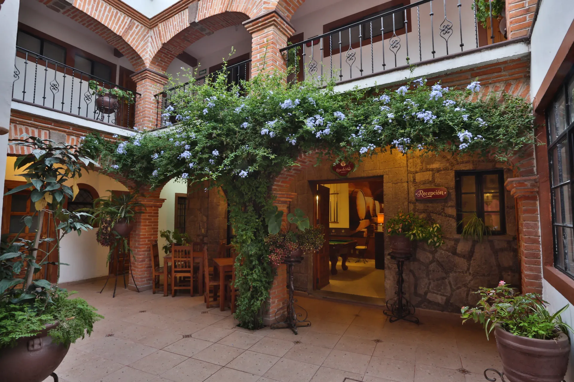 Courtyard restaurant with ivy-covered arches, potted plants, and warm-lit seating under an open balcony.