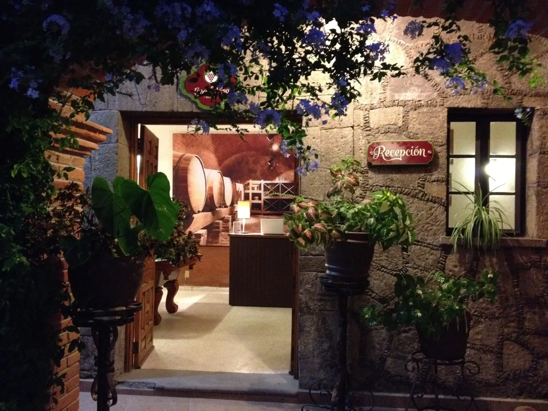 Dimly lit restaurant entrance with potted plants, warm interior glow, and a red sign by the door