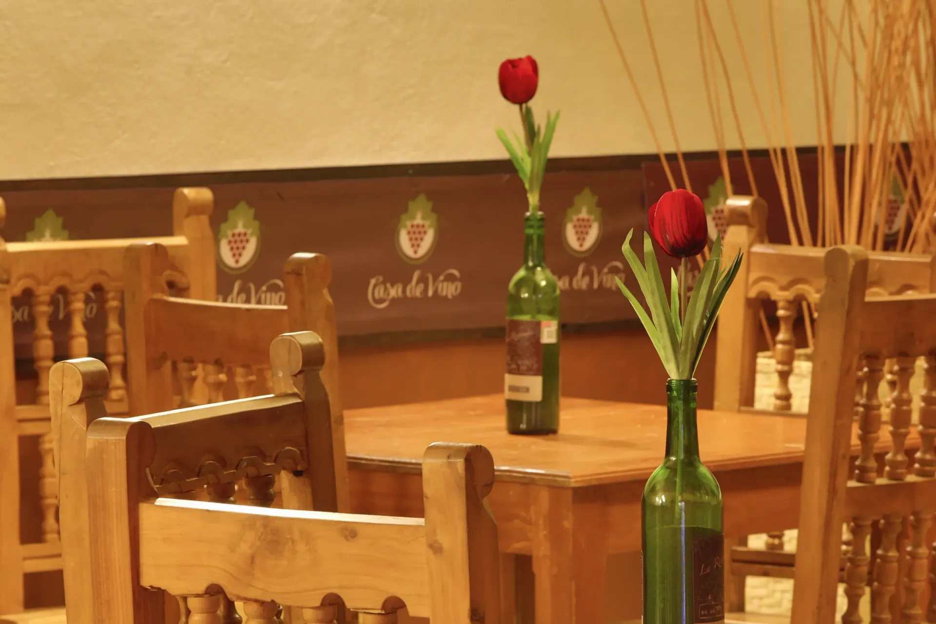 Wooden café tables and chairs with red tulips in green bottles under warm lighting