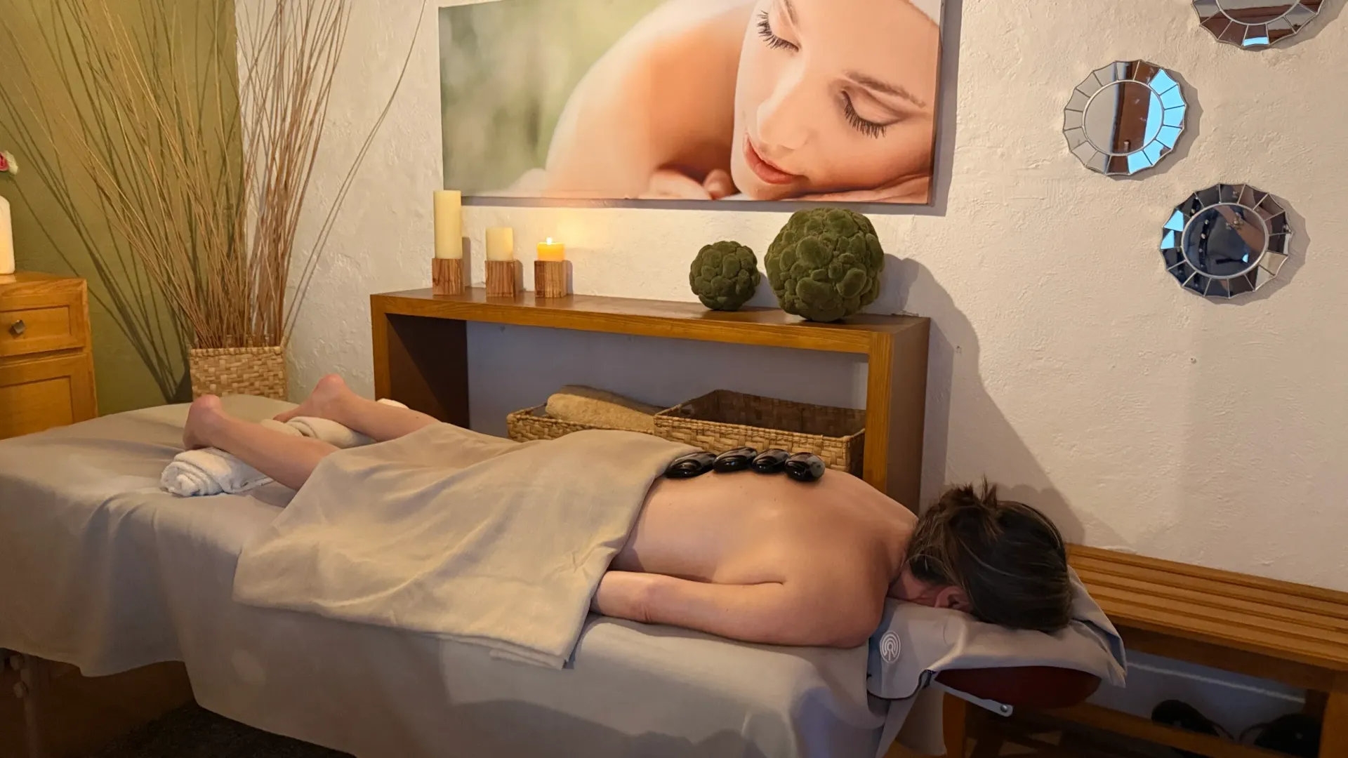 Sala de tratamientos de spa con una persona tumbada boca abajo en una camilla de masaje cubierta con una manta,