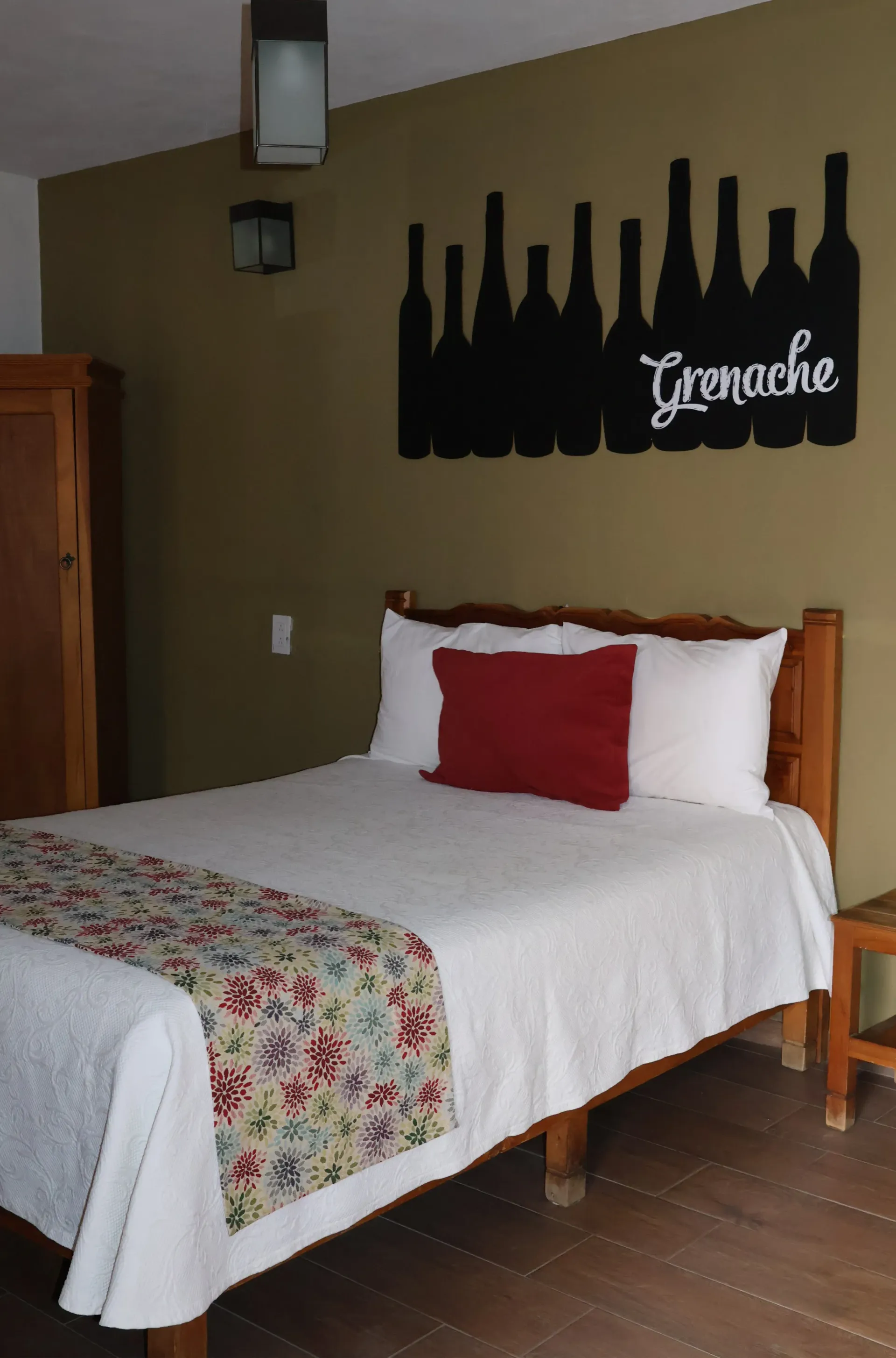 Cozy bedroom with a bed, red pillow, floral bed runner, and wall art of bottles above the headboard