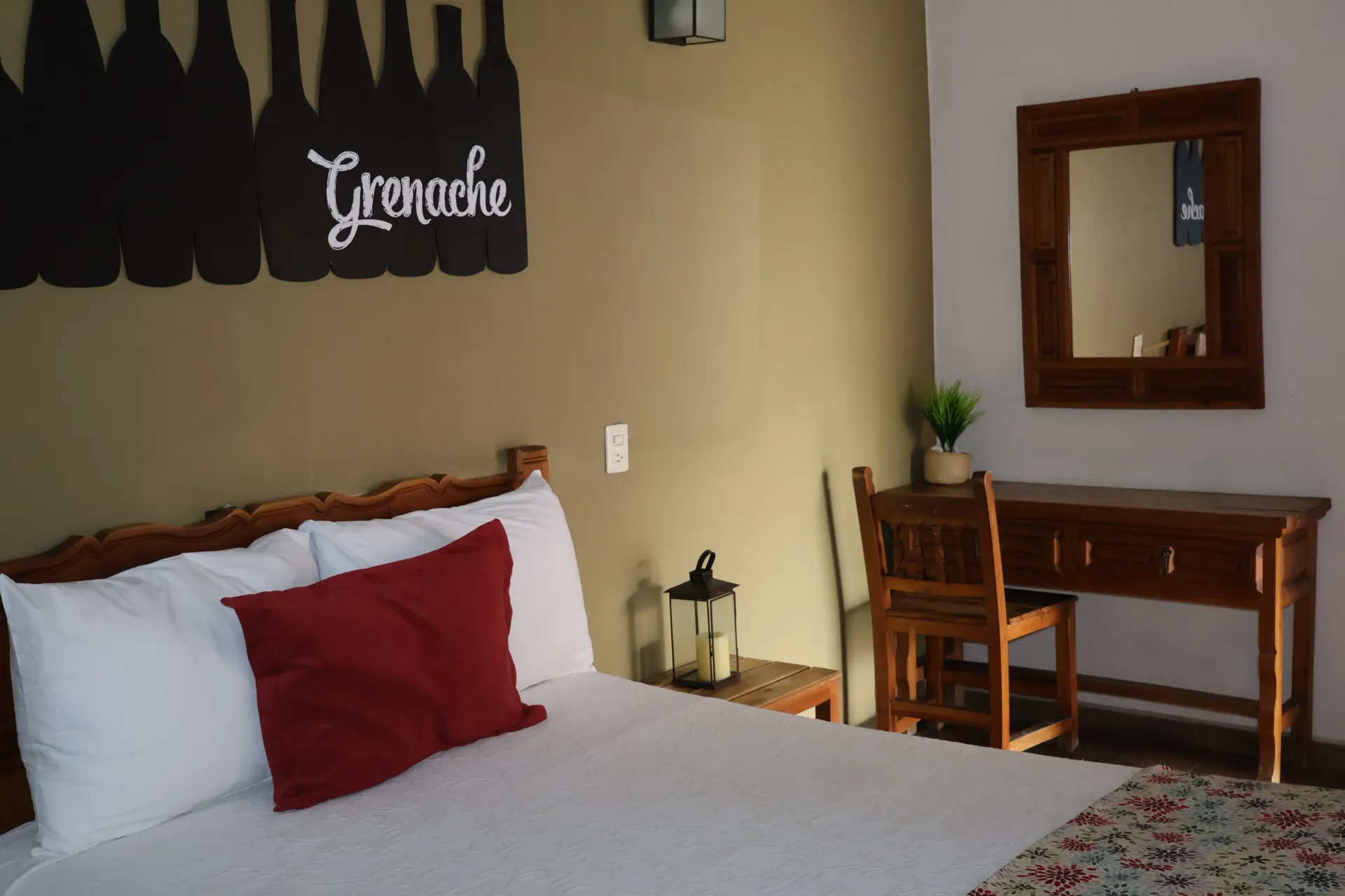 Cozy bedroom with a bed, red pillow, wooden desk, mirror, and lantern decor on beige walls