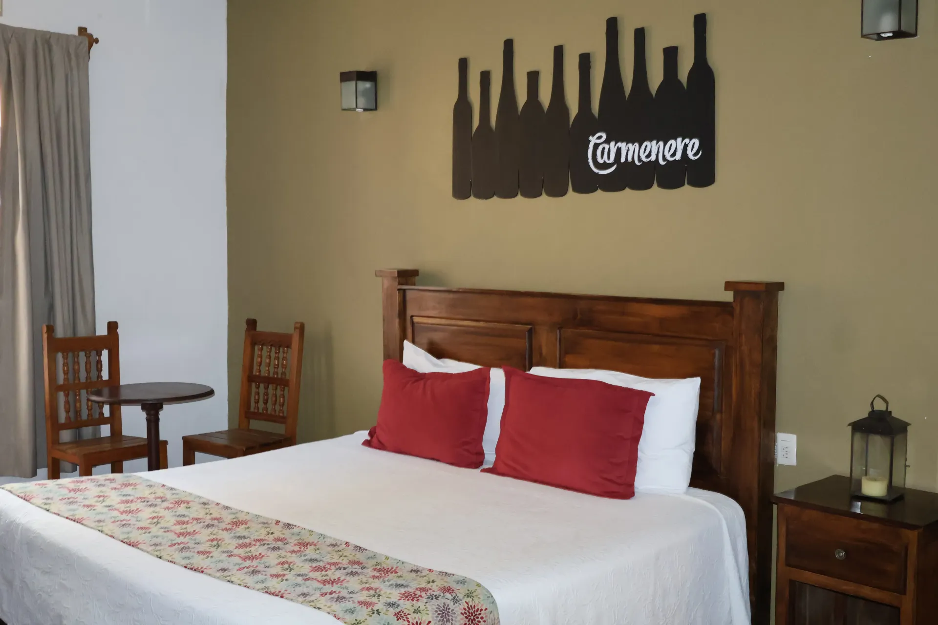 Hotel room with wooden bed, white linens, red pillows, and small table by the window