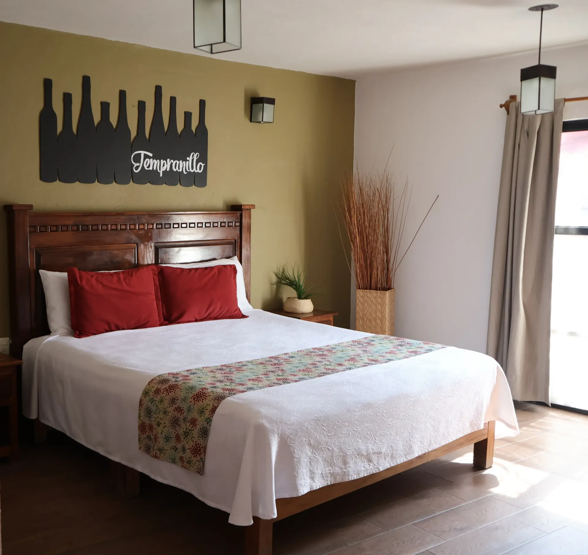 Habitación acogedora con cama de madera, almohadas rojas, paredes color canela y un cuadro con el perfil de la ciuda.