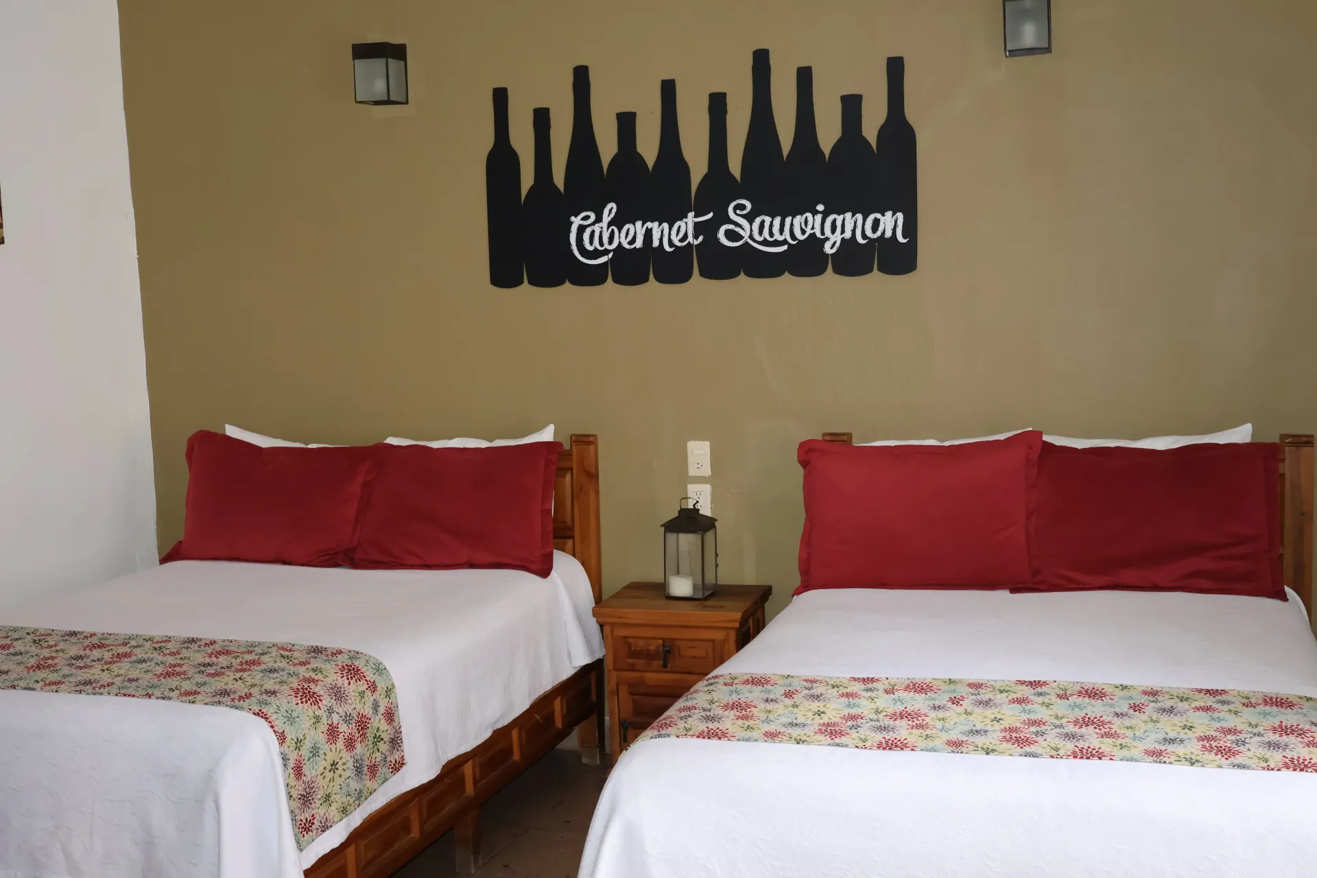 Two twin beds with red pillows in a beige hotel room, with a decorative wall sign above.