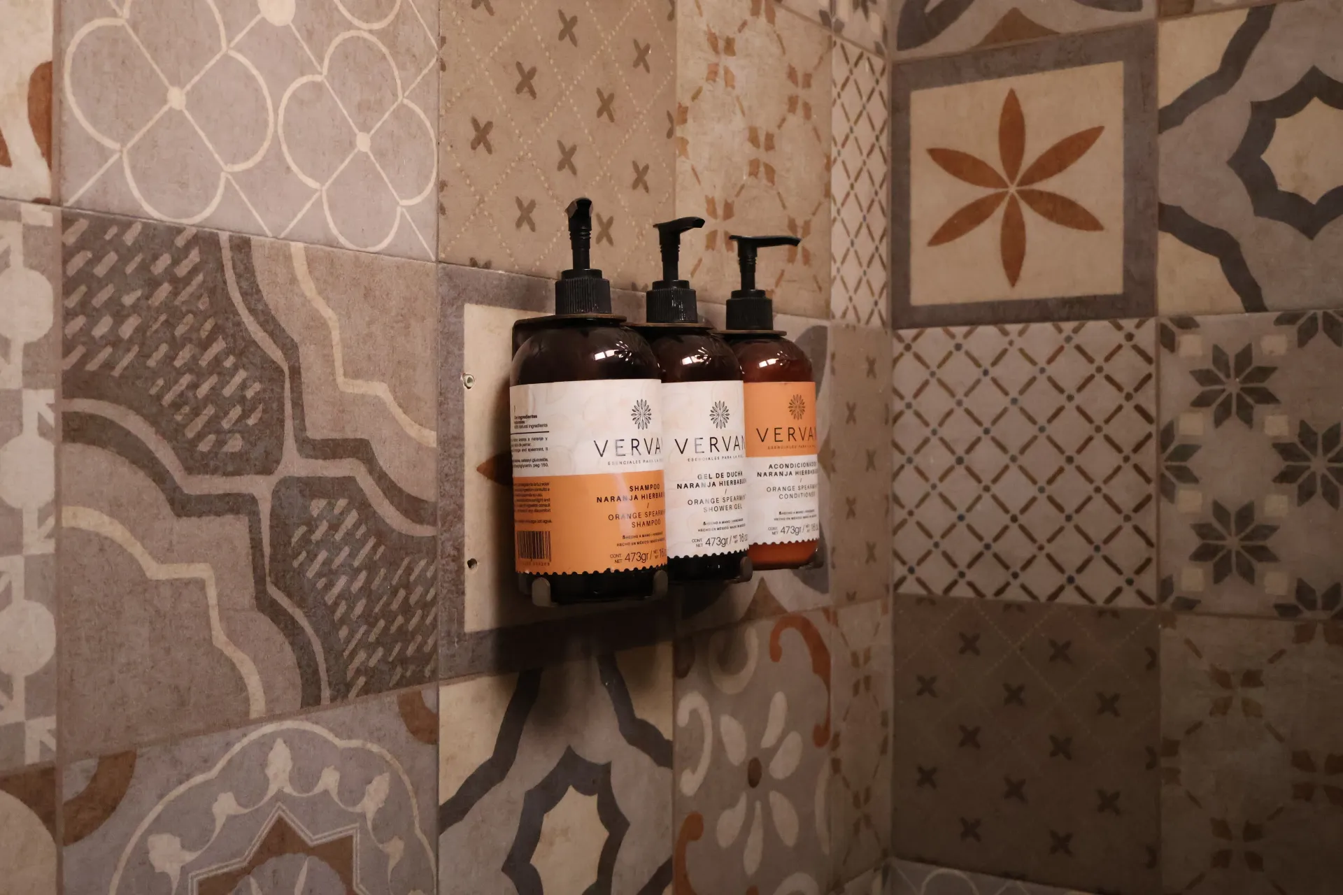 Three soap dispensers mounted on a patterned tile shower wall.