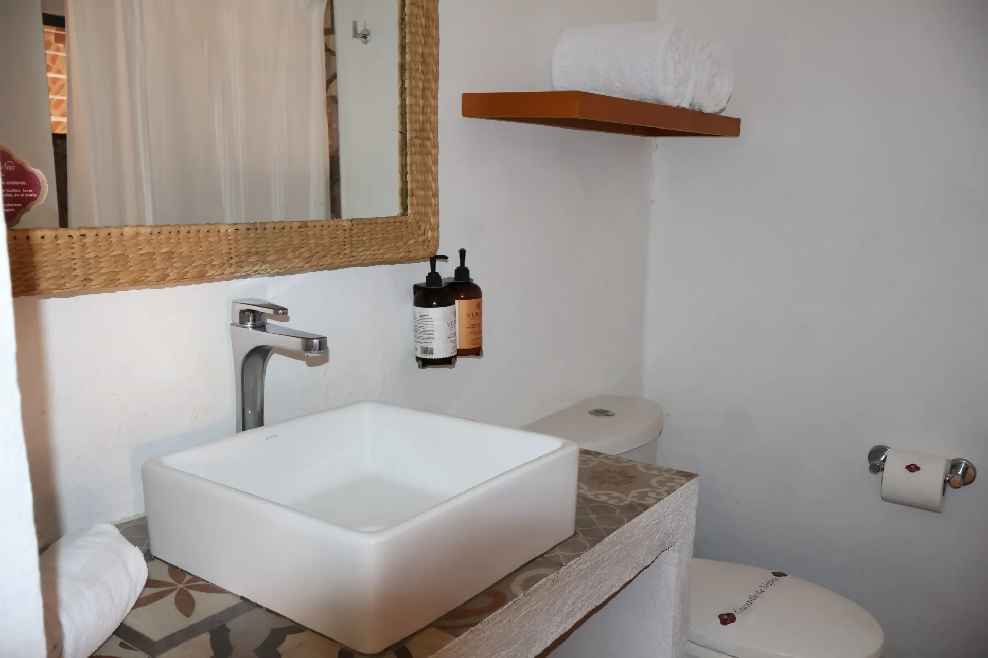 Modern bathroom with a white vessel sink, mirror, soap dispensers, and wall shelves