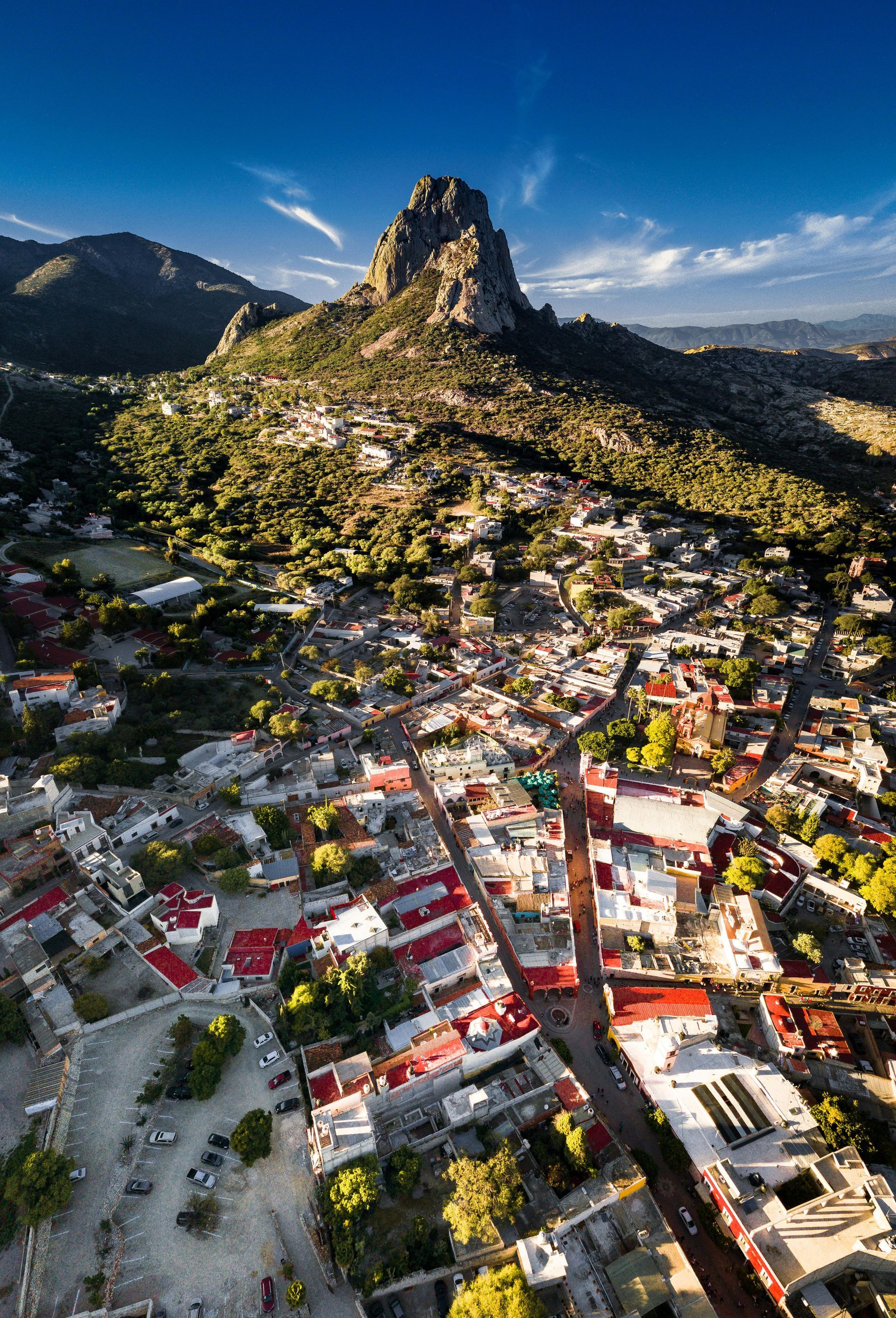 Aerial view of a colorful hillside town below a rocky mountain peak under a clear blue sky