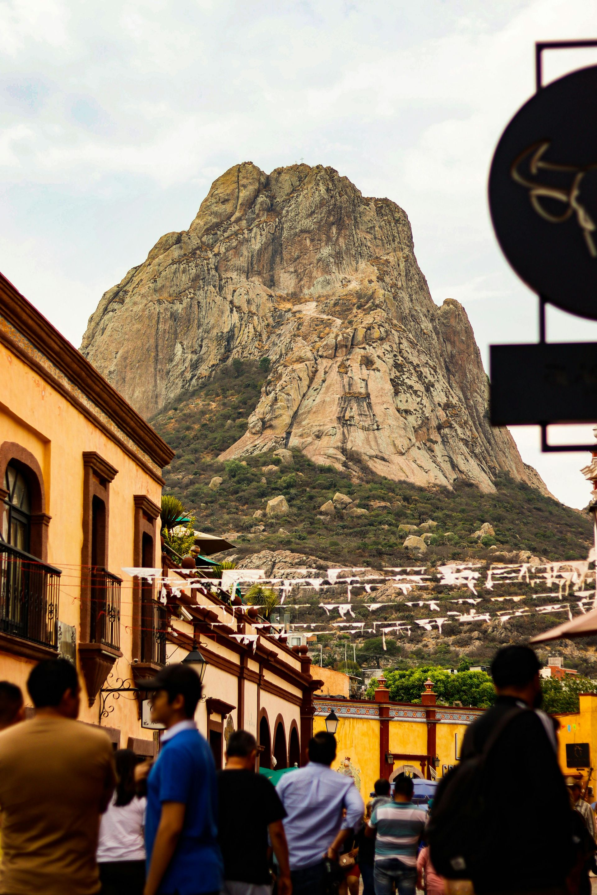 Escena callejera con peatones y edificios que conducen a una gran montaña rocosa al fondo.