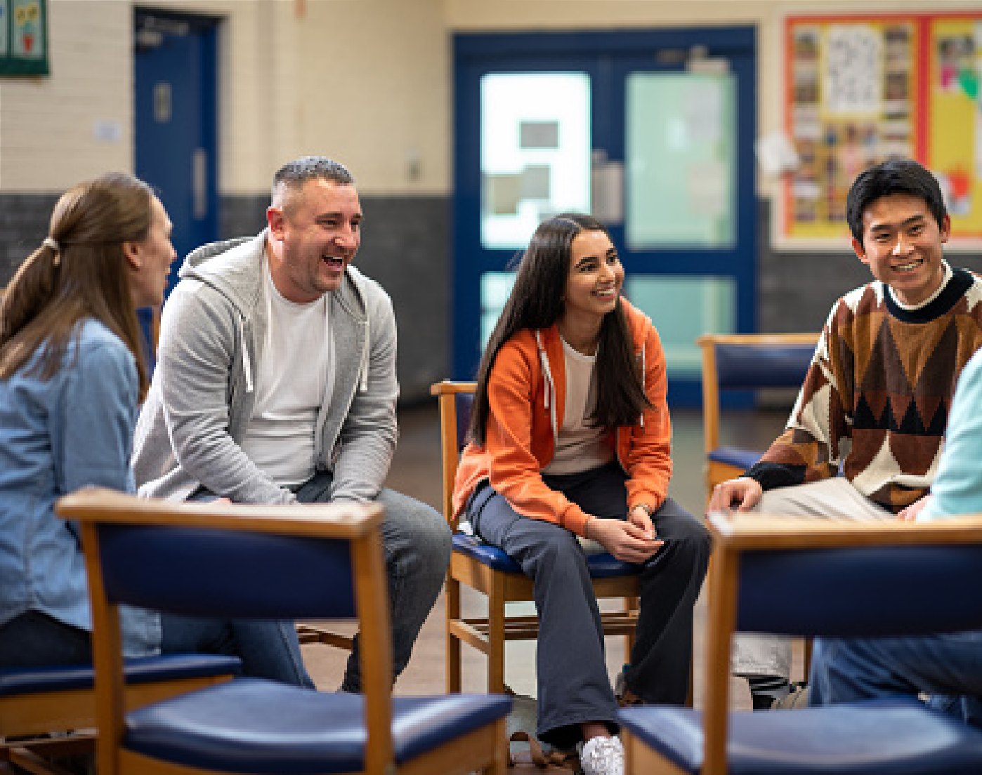 People sitting in a classroom in a circle, smiling and talking during a discussion.