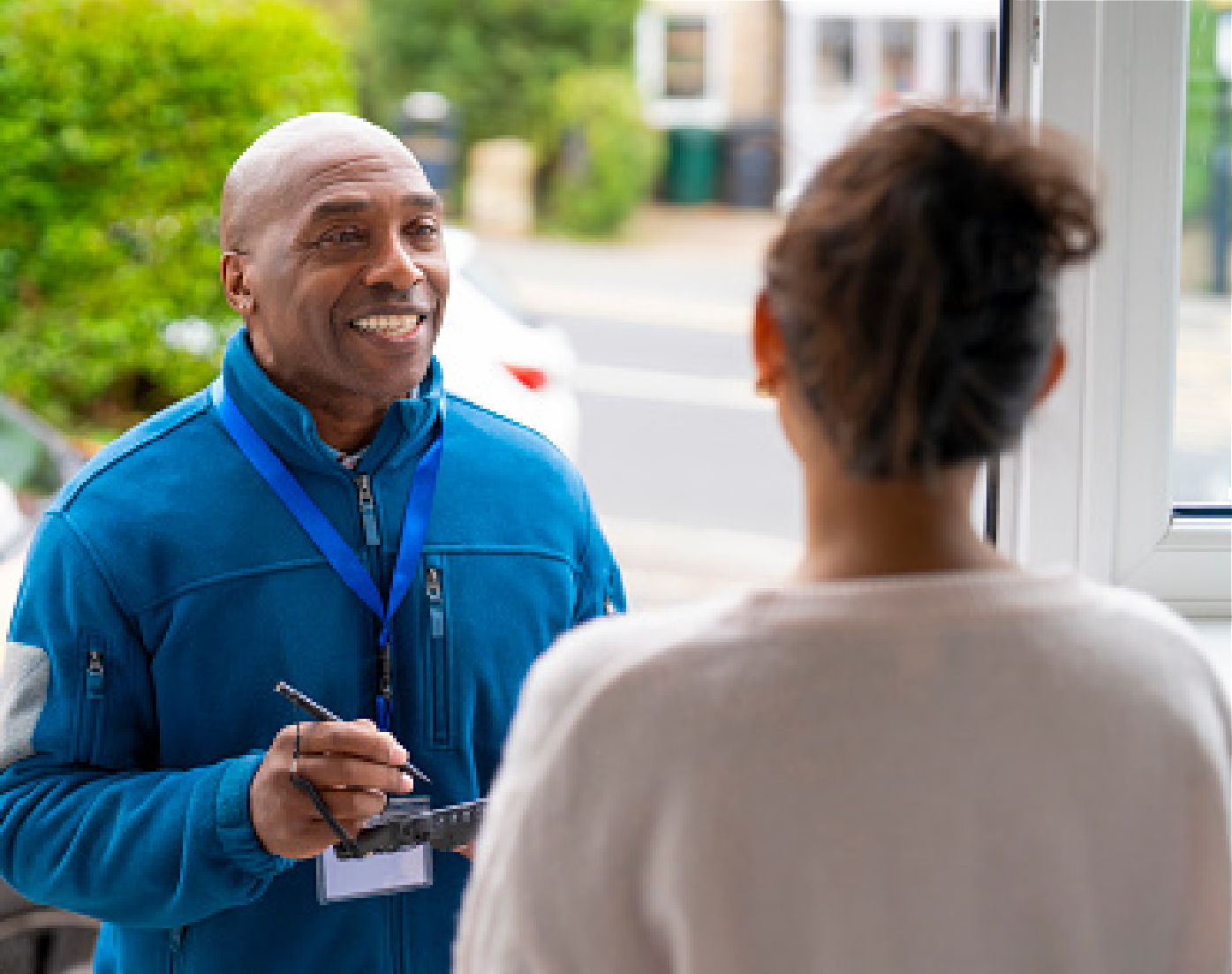 Delivery worker smiling and taking notes while speaking with a person at a doorway
