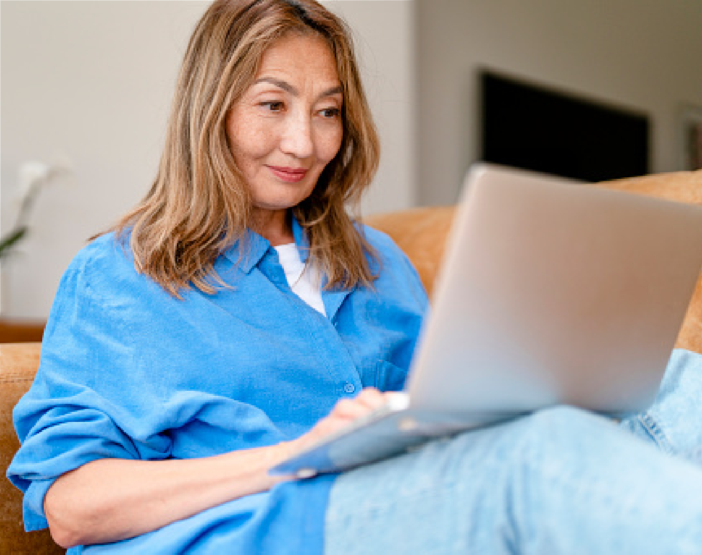 Woman in a blue sweater using a laptop on a couch