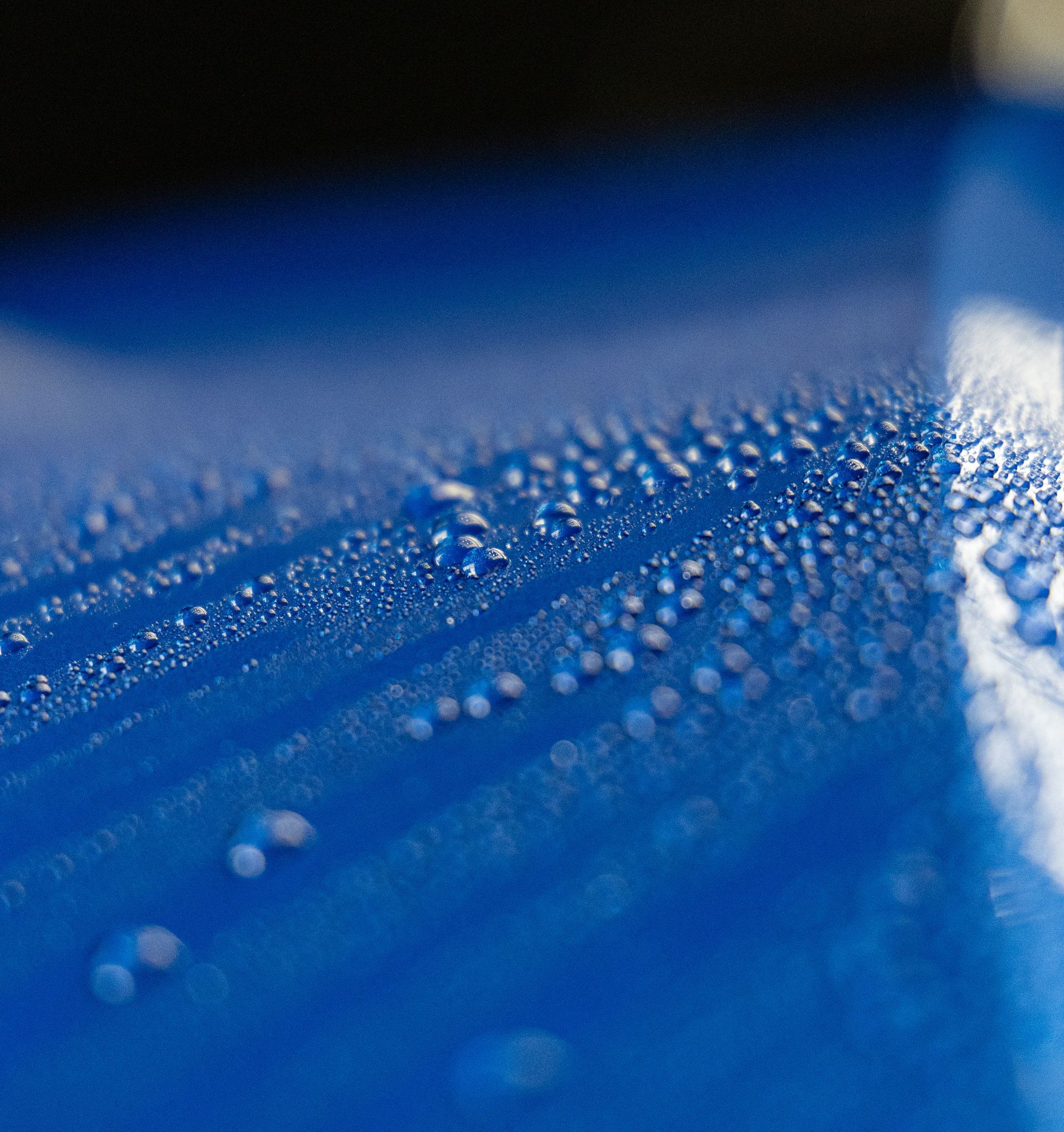 Close-up of blue fabric with water droplets and a blurred reflective edge