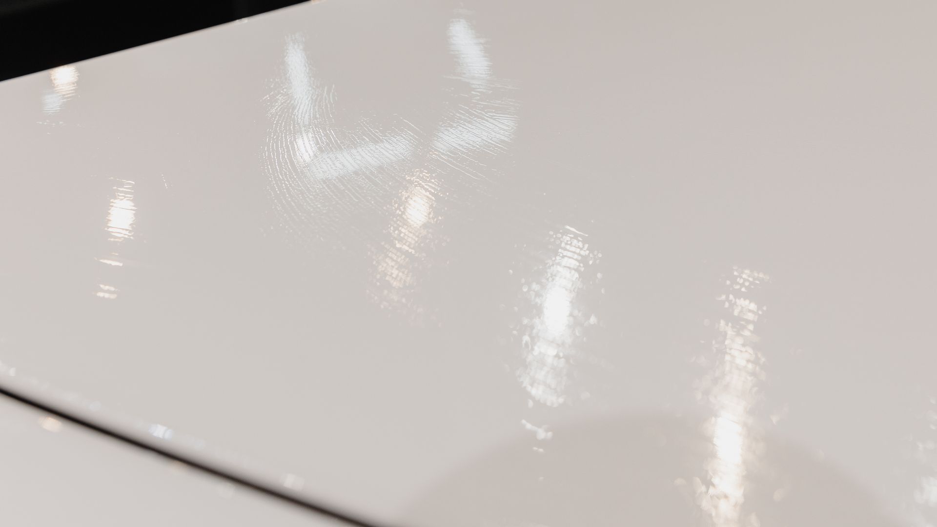 Glossy white car hood with bright reflections and a black seam line