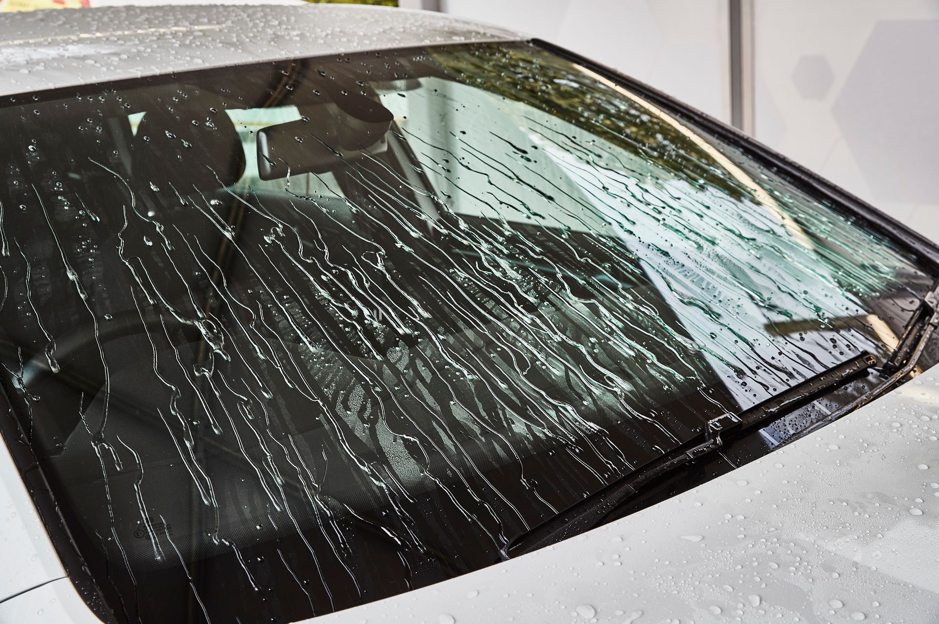 White car windshield shattered with cracks and water streaks, parked indoors.