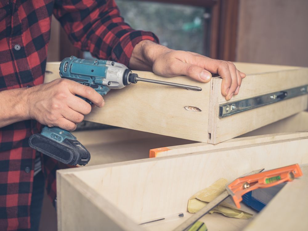 A Man Is Using A Drill To Drill A Hole In A Piece Of Wood — Damn Fine Constructions In Coffs Harbour, NSW
