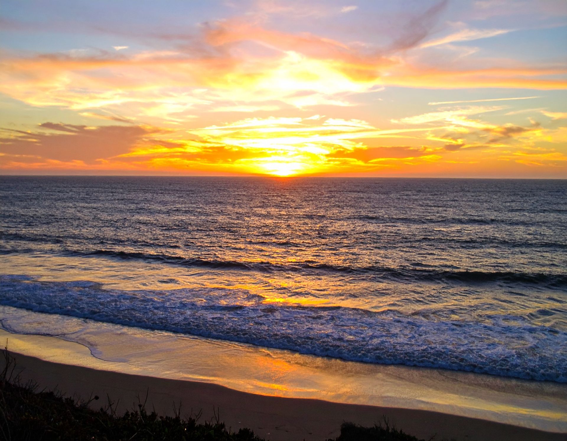 Sunset over ocean waves with golden sky and a dark sandy shore