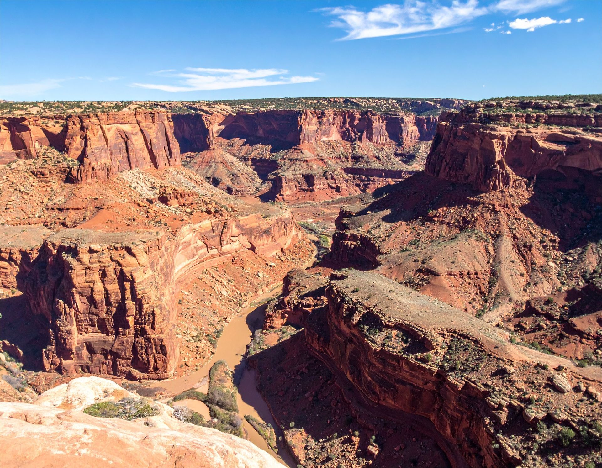 Sunlit red-rock canyon with a winding river below and blue sky above