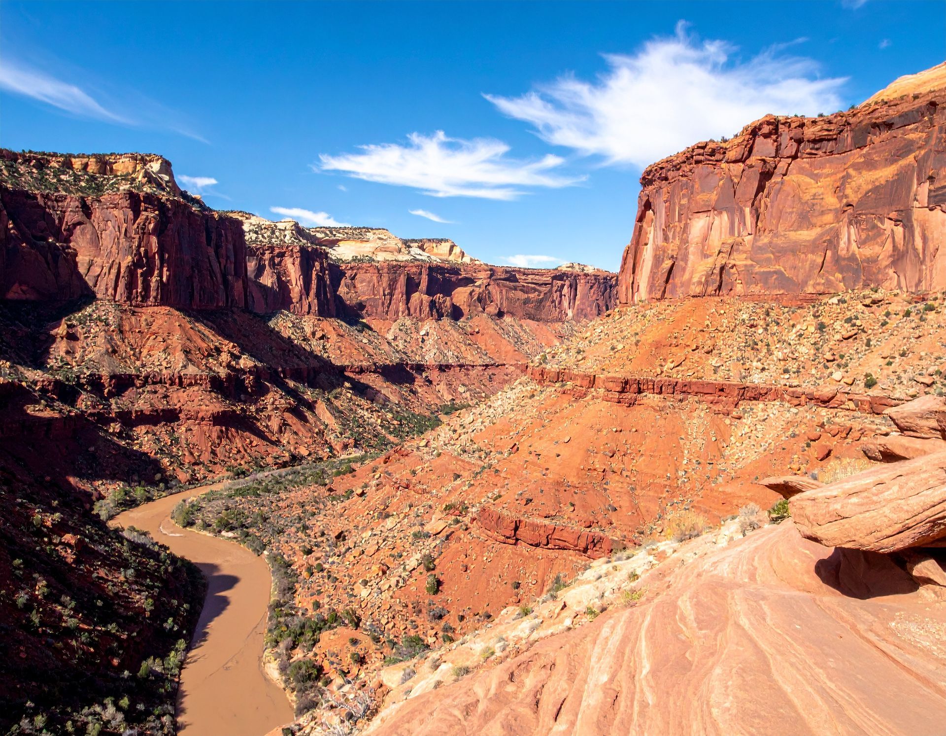Red canyon cliffs and a winding river under a bright blue sky in a desert landscape