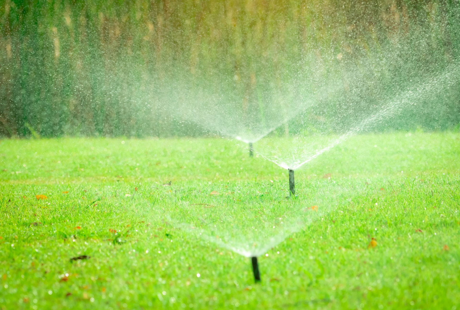 A sprinkler sprays water over a lush green field, creating a refreshing mist in the air A sprinkler sprays water over a lush green field, creating a refreshing mist in the air
