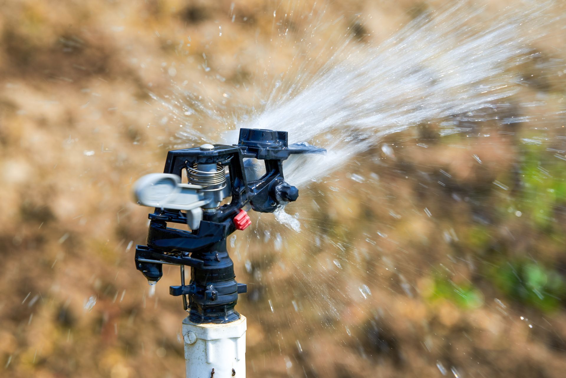 A close-up of a sprinkler actively spraying water across a field A close-up of a sprinkler actively spraying water across a field