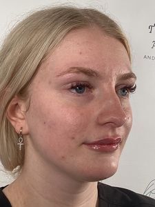 Close-up profile of a blonde woman wearing a cross earring, looking to the right against a light background