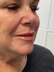 Close-up side profile of a woman smiling softly, wearing a dark top against a white tiled background