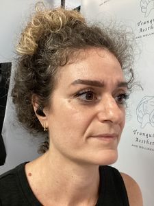 Side profile of a woman with curly hair wearing a black sleeveless top and earbuds against a gray background